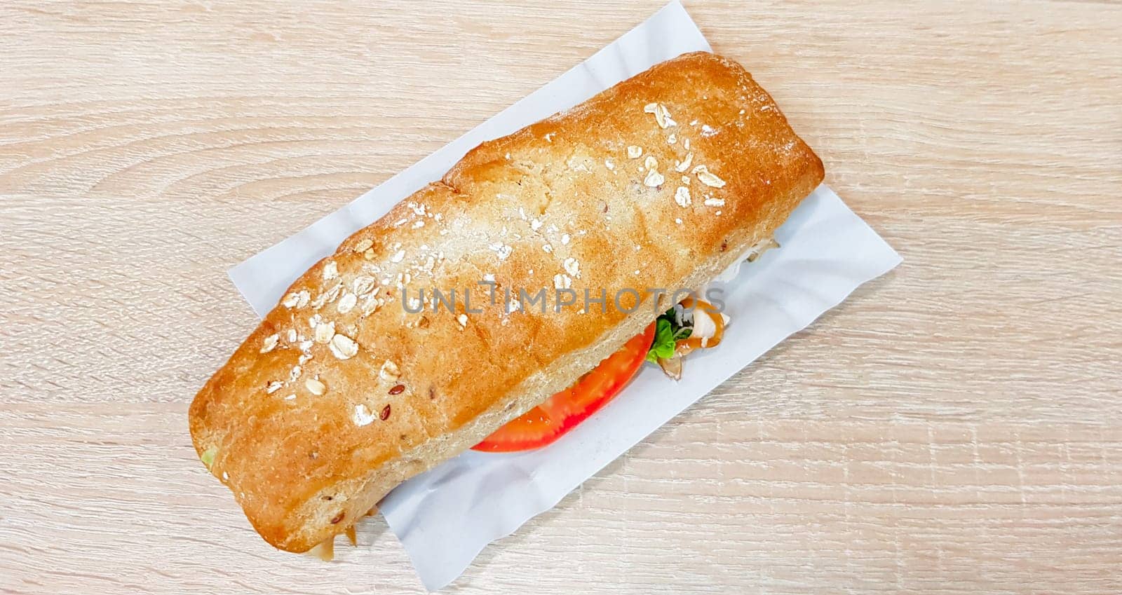 Ciabatta sandwich with lettuce, chicken and cheese on a wooden table.