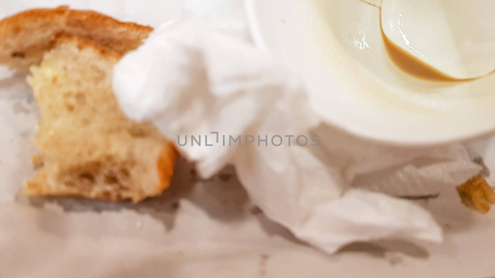 Leftover food on a paper plate and empty dirty paper coffee cup on a wooden table in a fast food cafe.