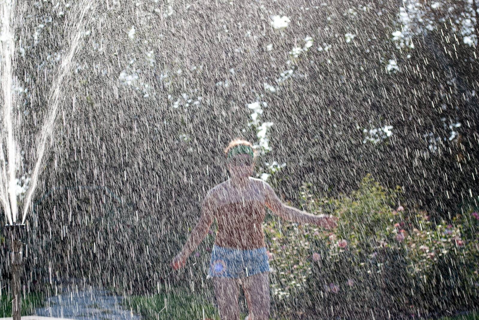 happy girl runs through a fountain in a green park in the sunshine.