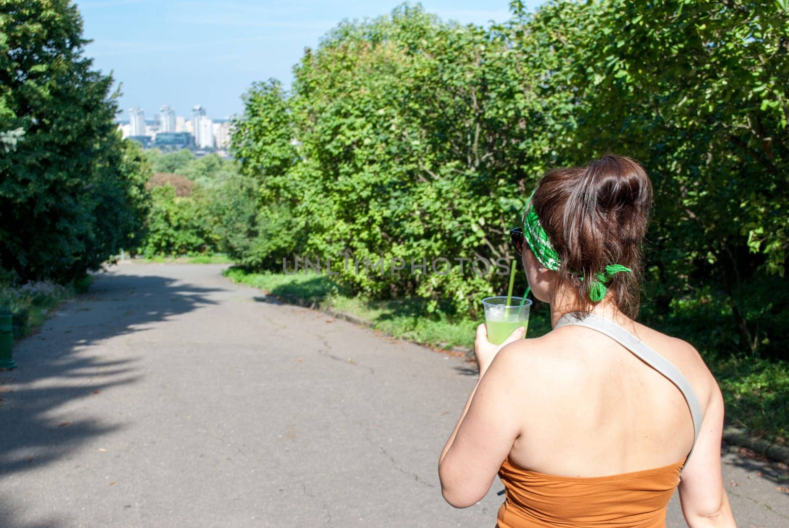 Young beautiful girl drinking a green drink from a plastic cup takeaway food. Summer cold drinks.