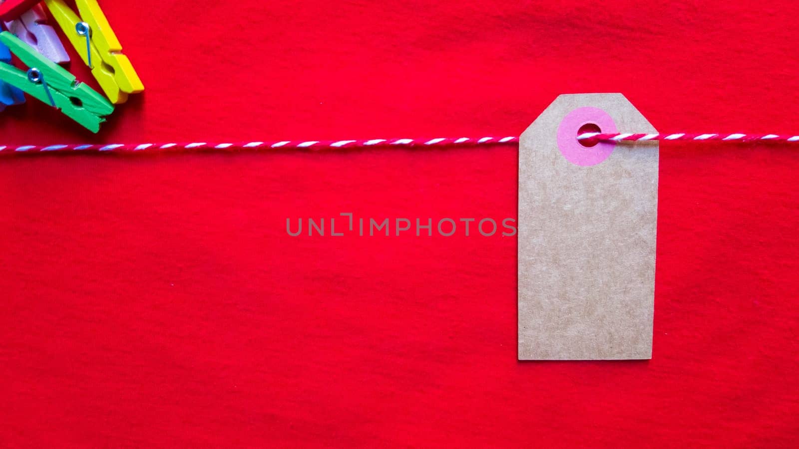 Colorful paper notes and clothespins on a red background. Empty color cardboard price tags, sale tag, gift tag, address label, luggage label hanging on clothes. Wooden clips. Layout, copy space for text, top view.