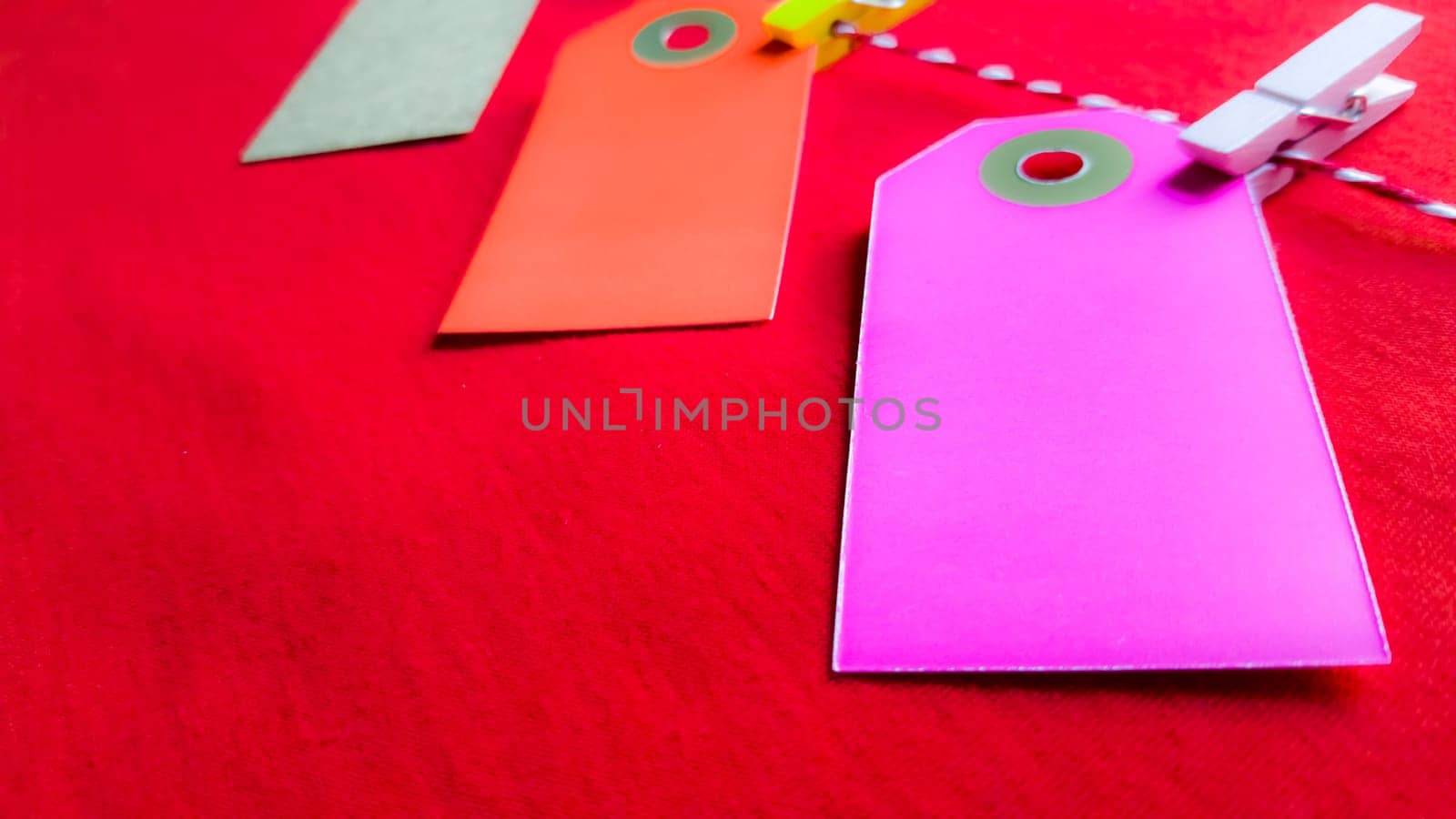 Colorful paper notes and clothespins on a red background. Empty color cardboard price tags, sale tag, gift tag, address label, luggage label hanging on clothes. Wooden clips. Layout, copy space for text, top view.