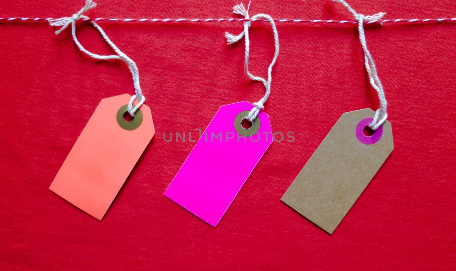 Three colored bright tags hang on a red rope on a red background. Copy space, place for text, flat lay