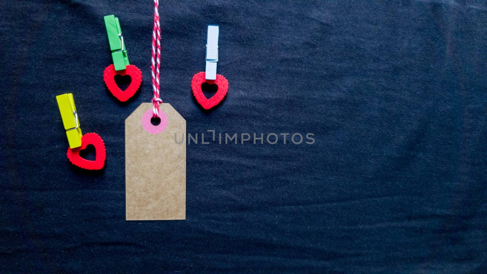 Natural blank old paper, fabric tag or label isolated on a dark background with a wooden red decorative heart. Holiday Valentine's Day, Black Friday, Christmas, New Year, birthday present for your beloved and beloved man or woman.