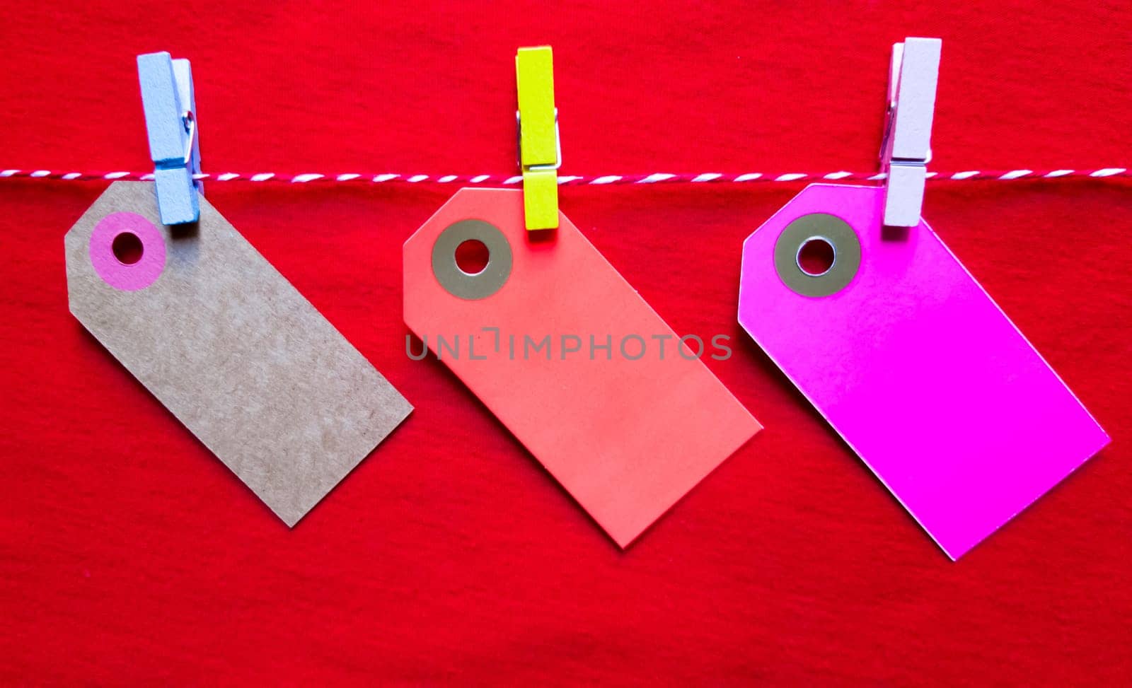 Colorful paper notes and clothespins on a red background. Empty color cardboard price tags, sale tag, gift tag, address label, luggage label hanging on clothes. Wooden clips. Layout, copy space for text, top view.