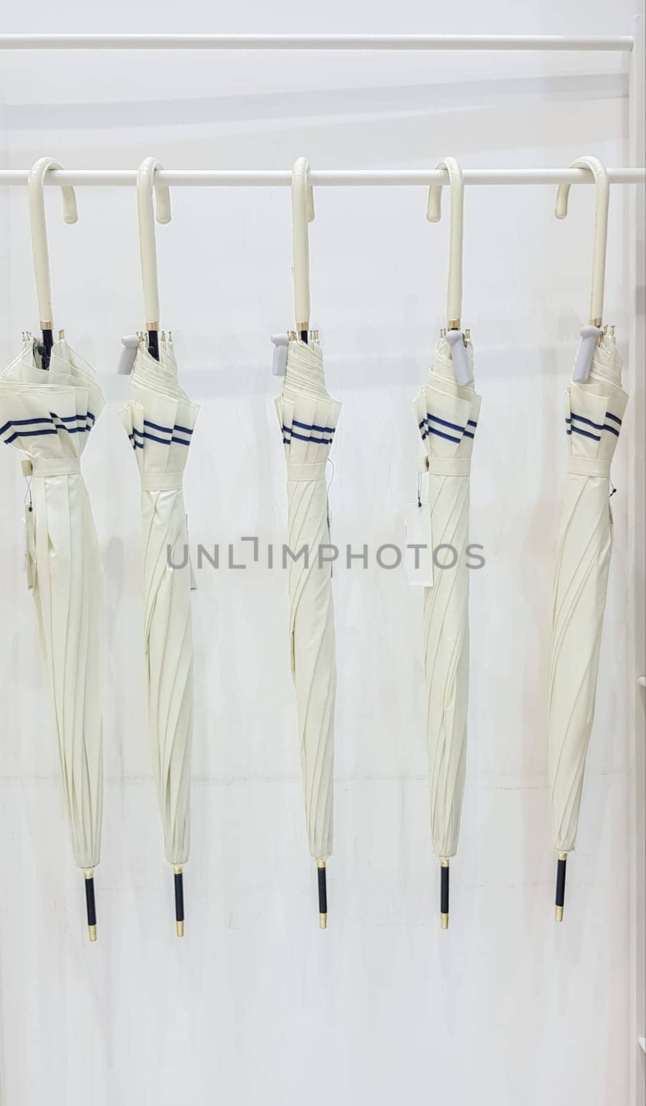 Five beige umbrellas hang on a coat hook hook, white background. Getting ready for the rainy season. Five modern umbrellas in a rack hanging in a white clothes hanger