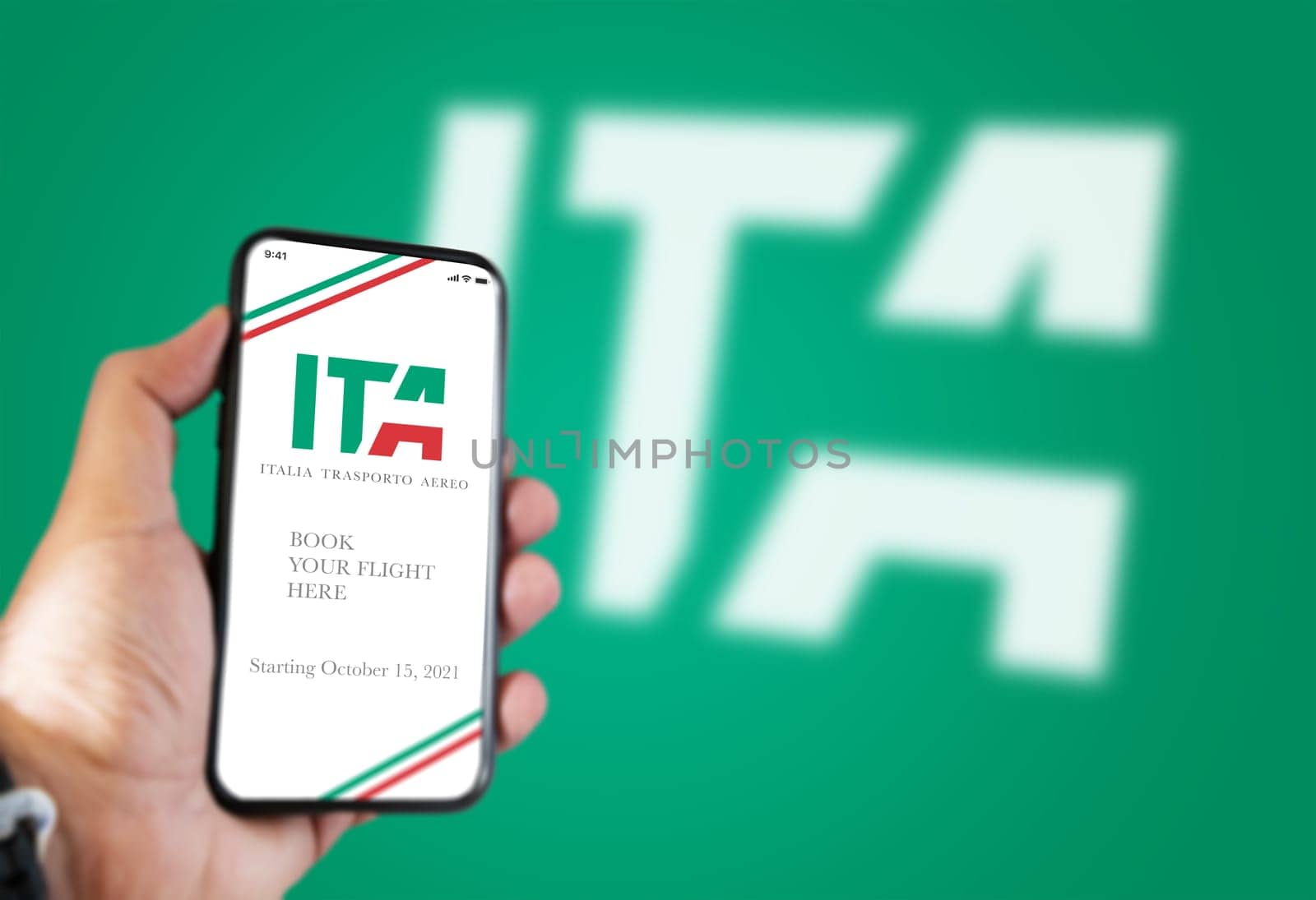 Rome, Italy, july 2021: A hand holding a phone with the ITA app on the screen and the ITA logo Blurred on a green background.ITA is the new Italian flag carrier starting from 15 October 2021