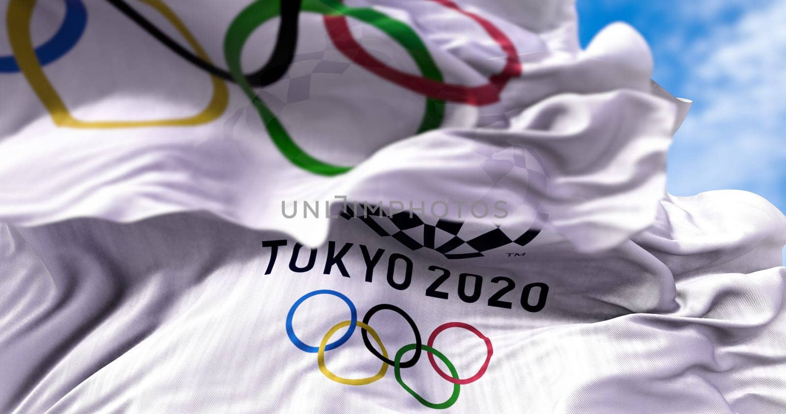 Tokyo, Japan, July 2021: Tokyo 2020 olympic flag waving with the Olympic flag blurred in the foreground. Selective focus. Tokyo 2020 olympics games were postponed to 2021 due to the covid-19 pandemic