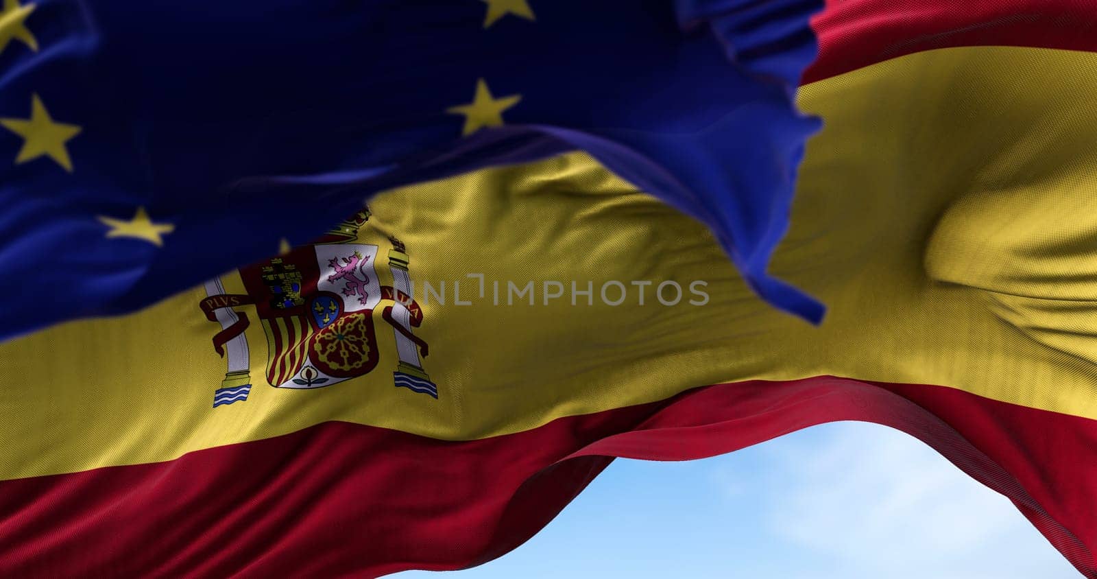 The national flag of Spain waving in the wind together with the European Union flag blurred in the foreground. Politics and finance. Spain is a member state of the European Union