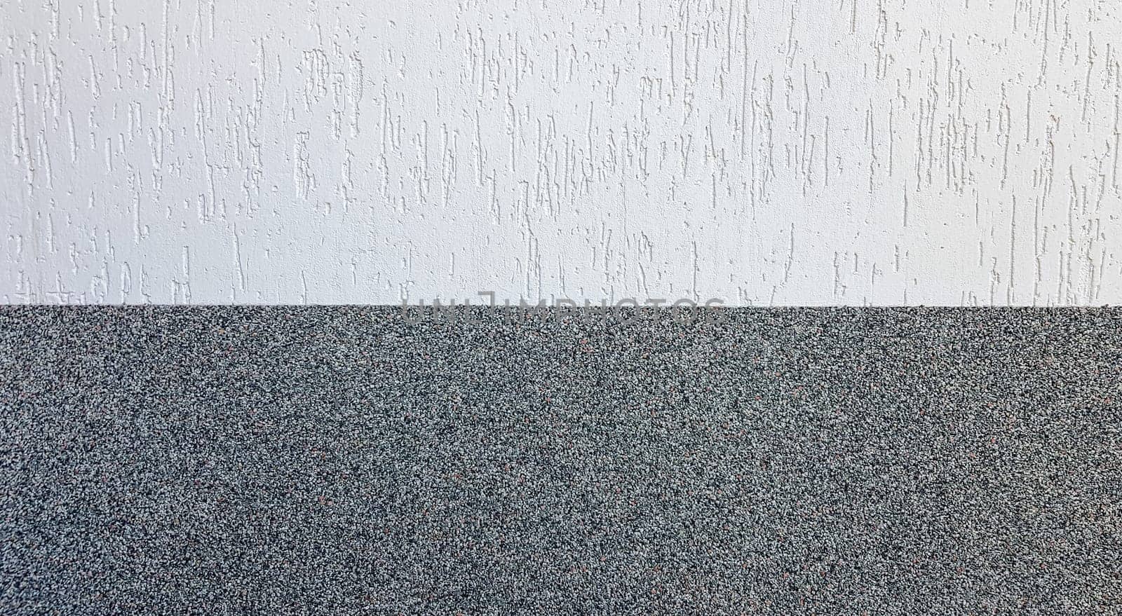Gray marble chips and decorative light stucco on the wall divided by a horizontal line. Building facade background. Stucco texture on the street.