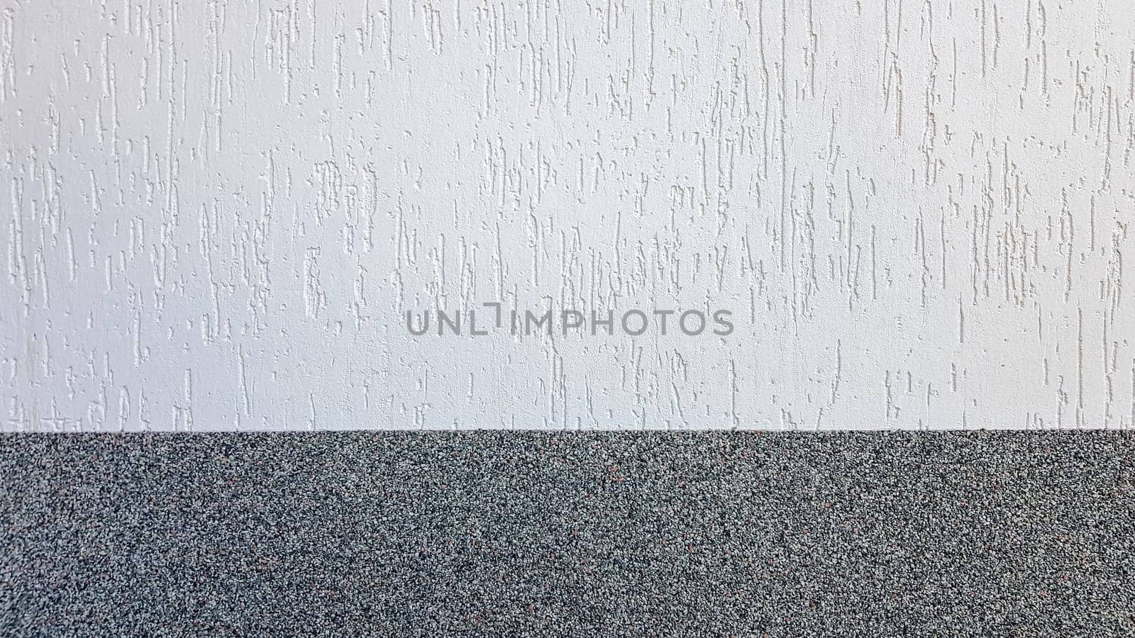 Gray marble chips and decorative light stucco on the wall divided by a horizontal line. Building facade background. Stucco texture on the street.