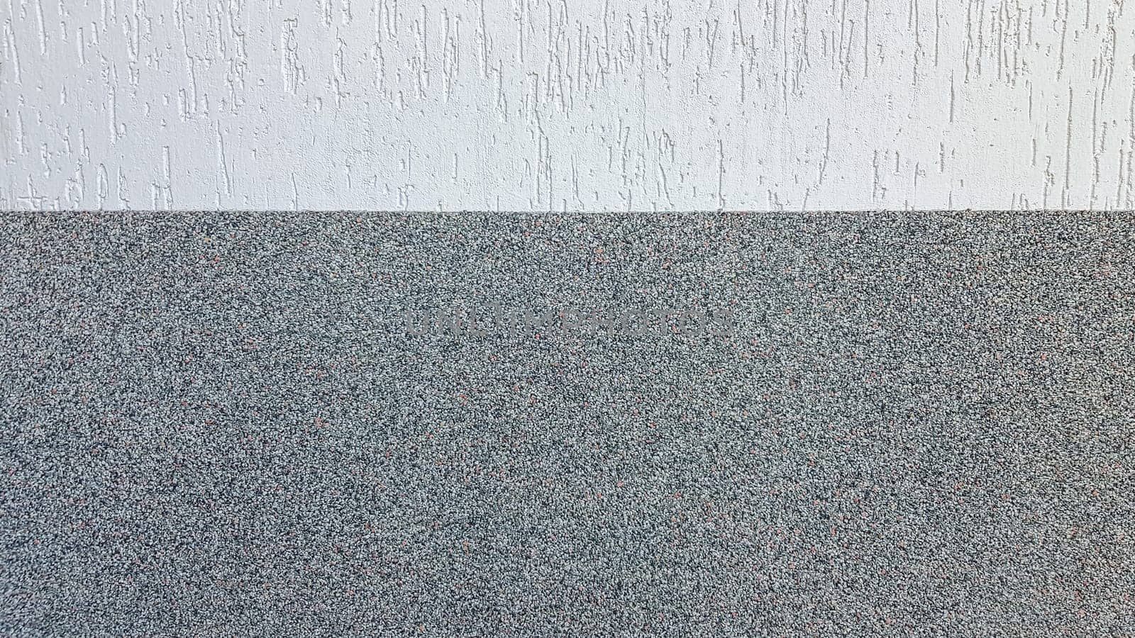 Gray marble chips and decorative light stucco on the wall divided by a horizontal line. Building facade background. Stucco texture on the street.