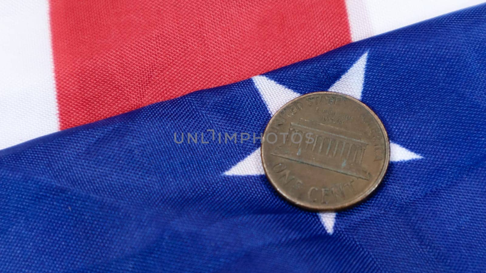 A 1 cent American dollar coin lies on the American flag. The currency is one cent over the flag of the United States