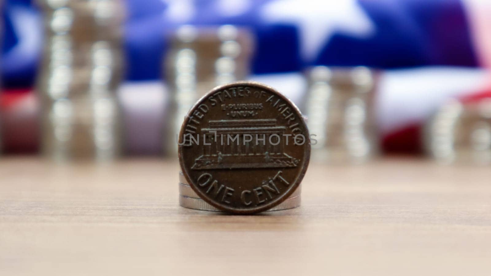 A 1 cent American dollar coin lies on the American flag. The currency is one cent over the flag of the United States