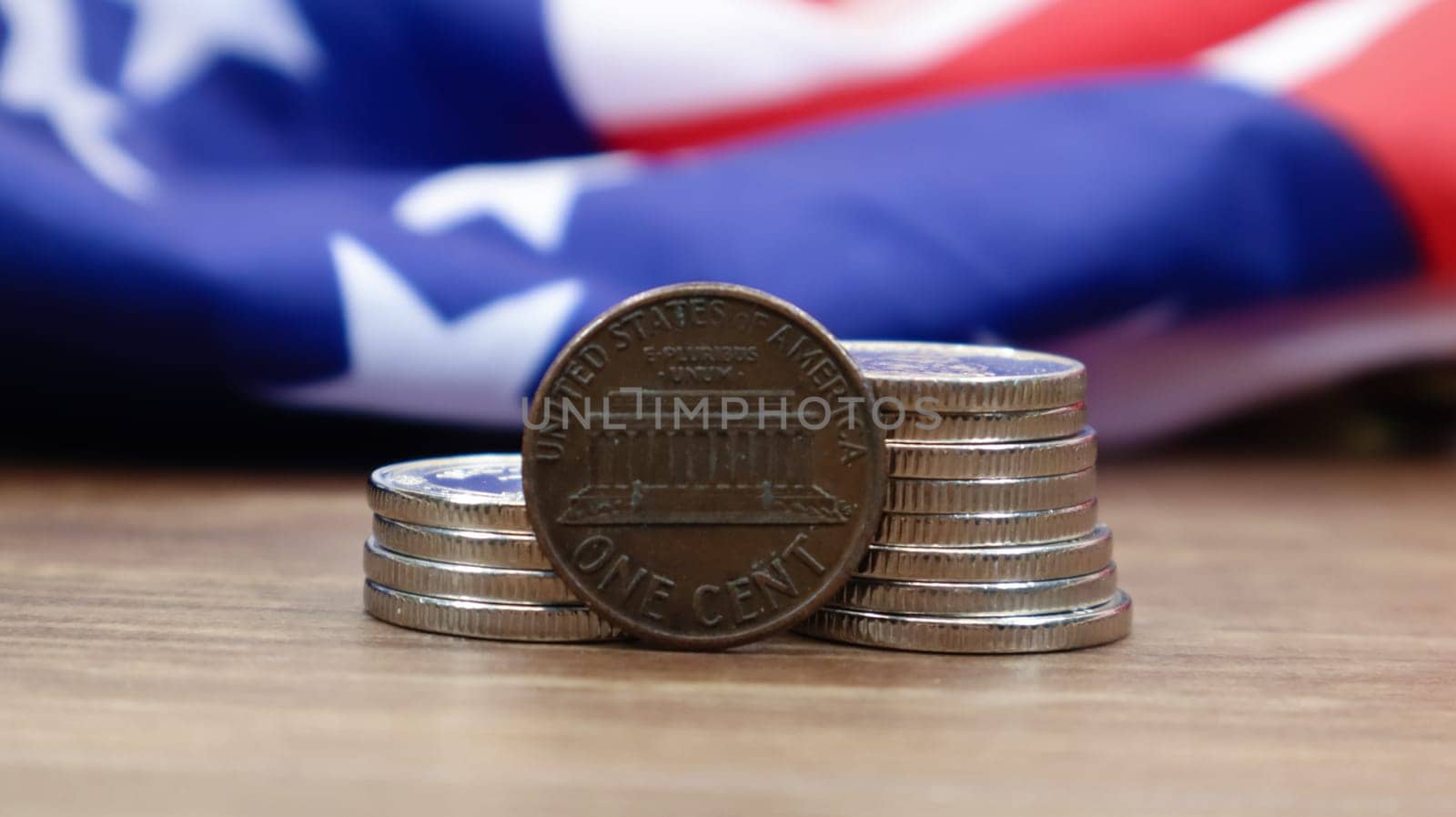 A 1 cent American dollar coin lies on the American flag. The currency is one cent over the flag of the United States