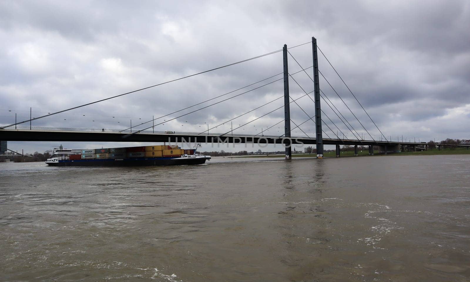 Germany, Dusseldorf - February 20, 2020: A loaded vessel in containers floats along the Rhine and under the Oberkassel bridge in the center of Dusseldorf. The ship goes against mating in the city.