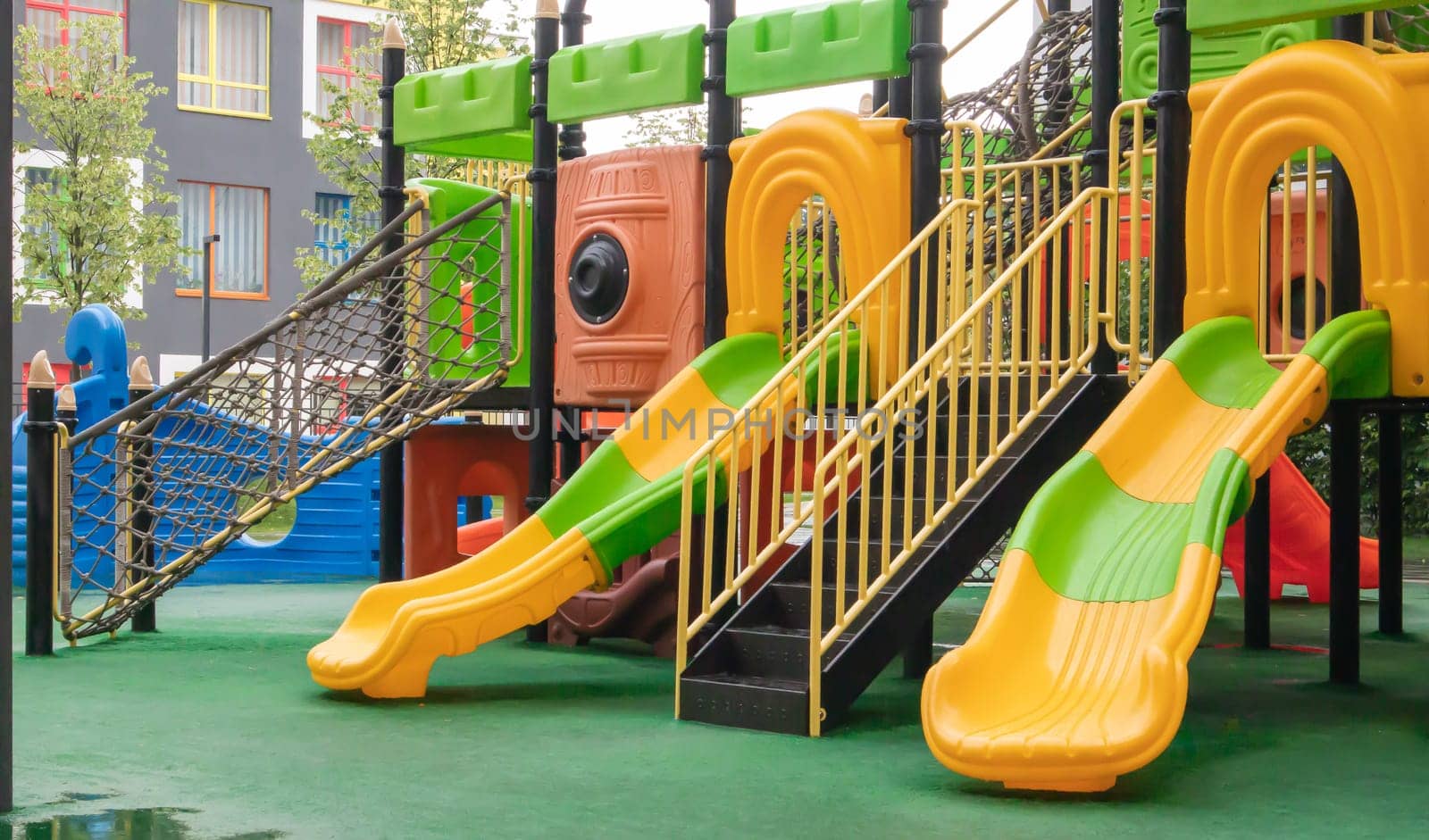 A courtyard of high-rise buildings with a new modern colorful and large playground on a rainy summer day without people. Empty outdoor playground. A place for children's games and sports