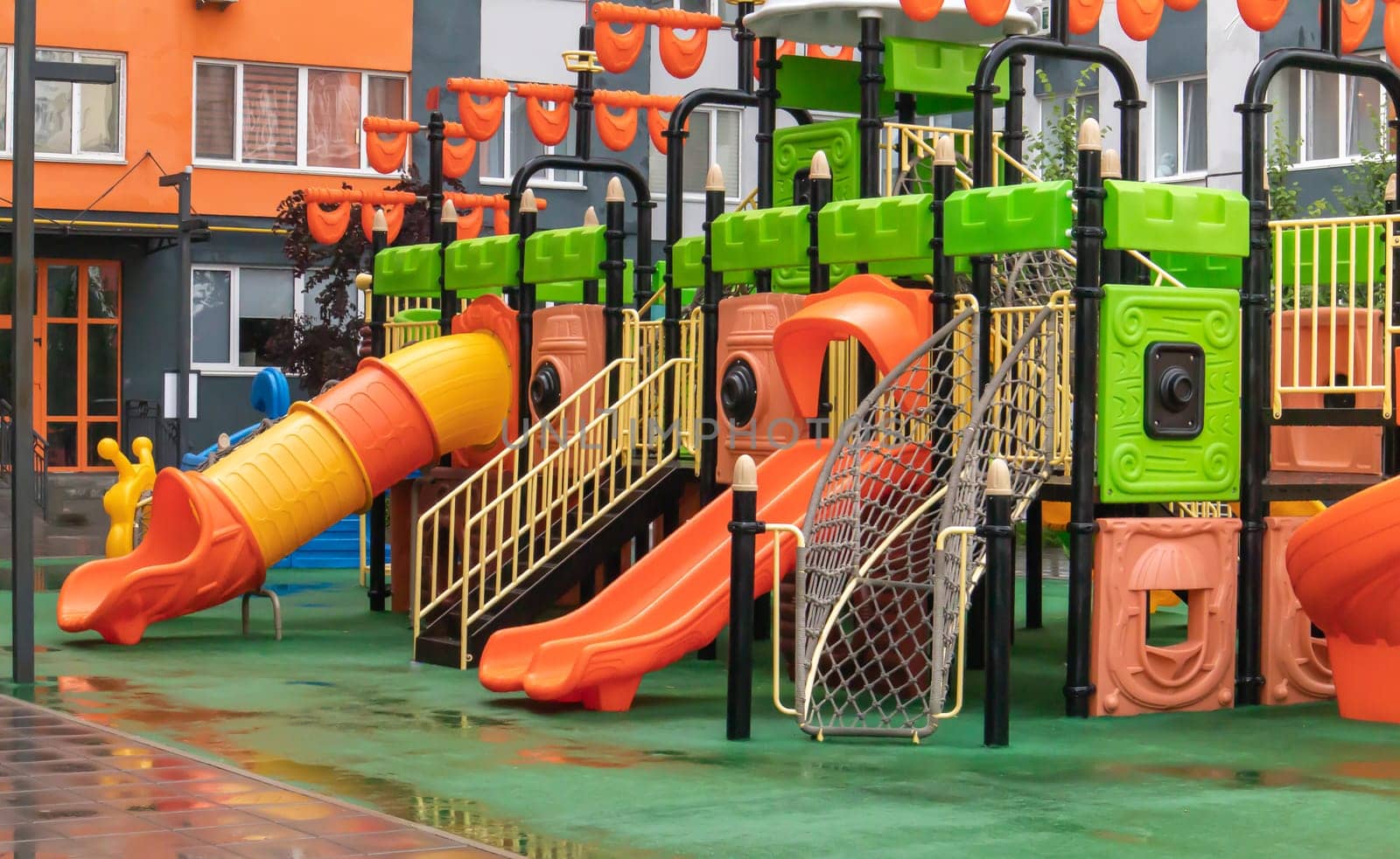 A courtyard of high-rise buildings with a new modern colorful and large playground on a rainy summer day without people. Empty outdoor playground. A place for children's games and sports