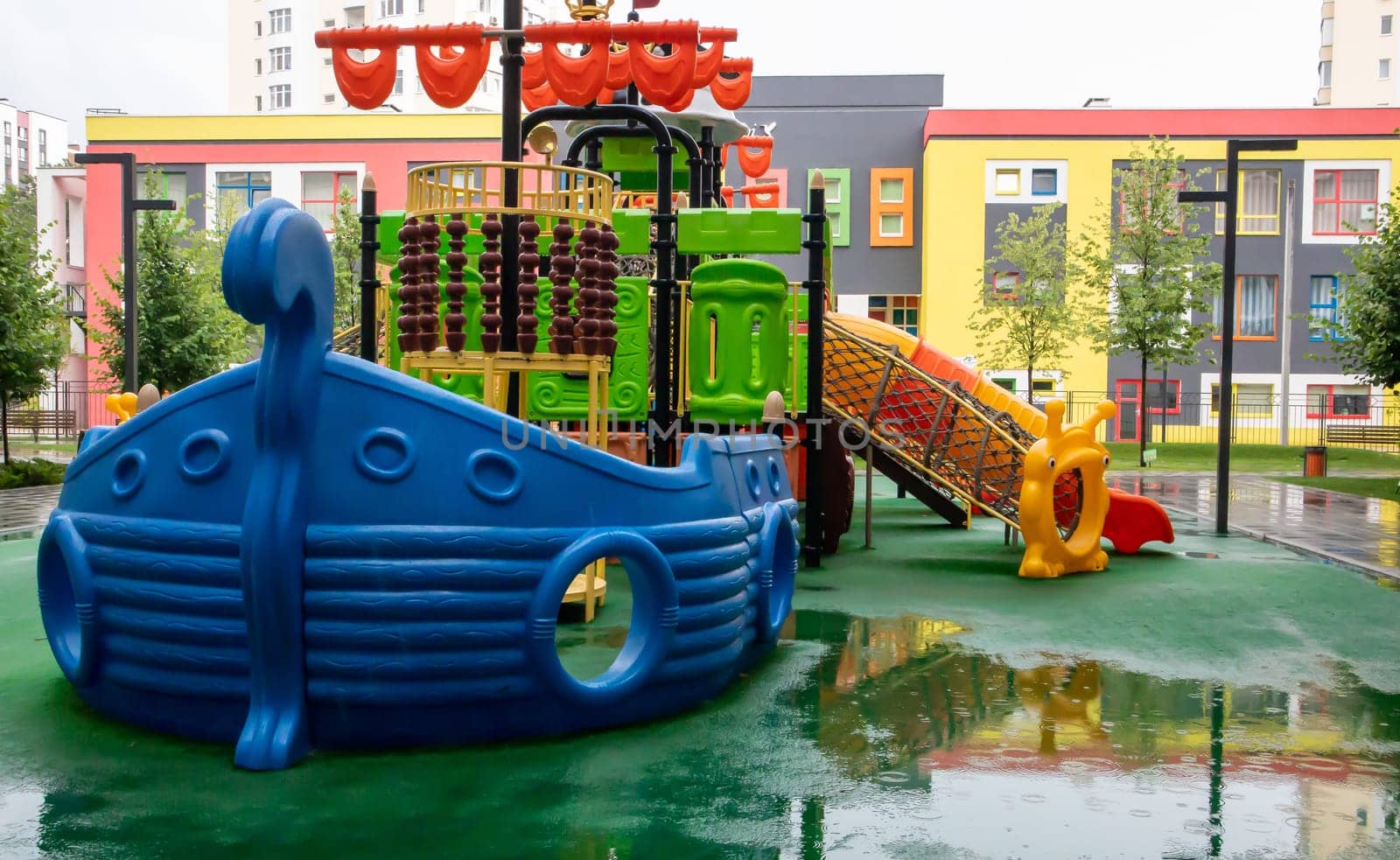 A courtyard of high-rise buildings with a new modern colorful and large playground on a rainy summer day without people. Empty outdoor playground. A place for children's games and sports