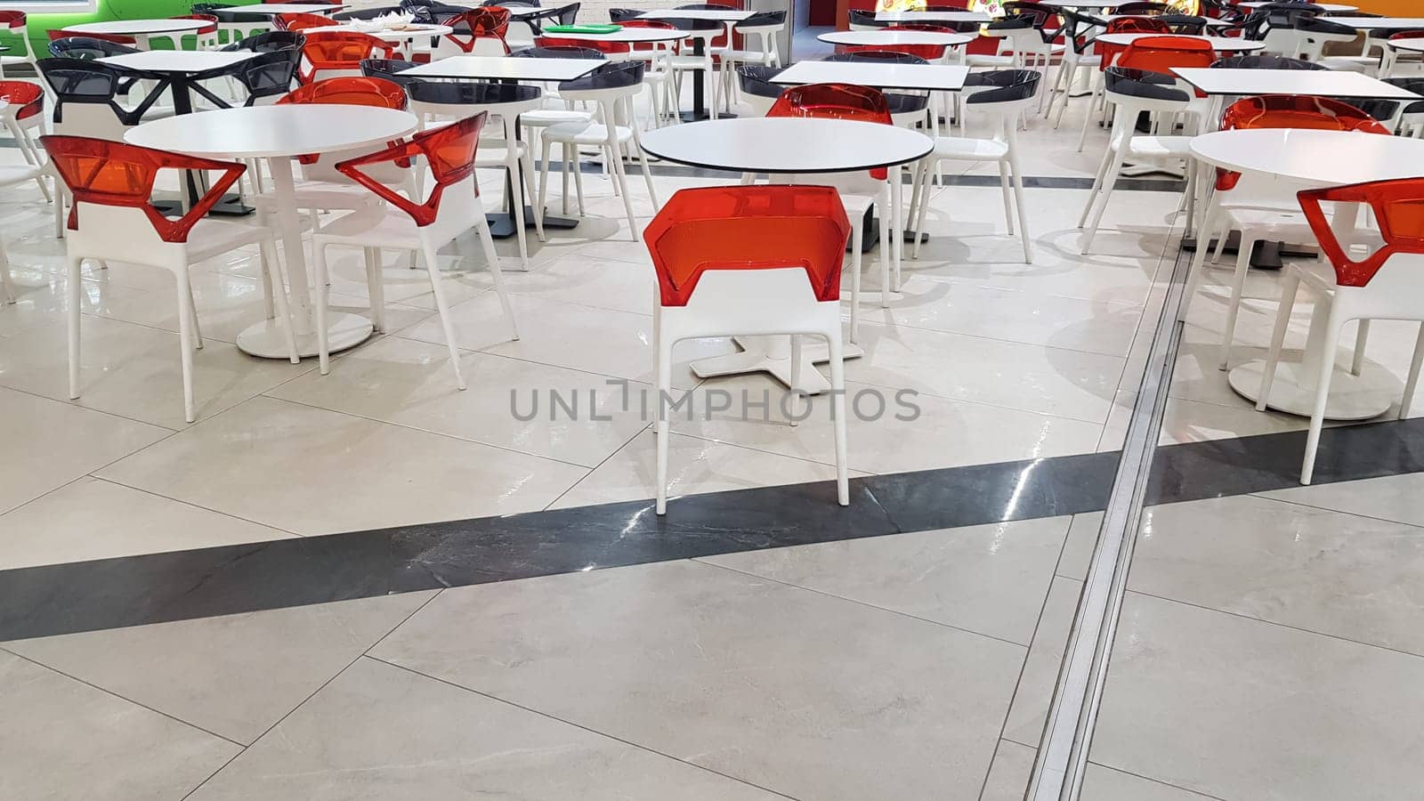 food area with plastic white and red tables and chairs in a mall without people.