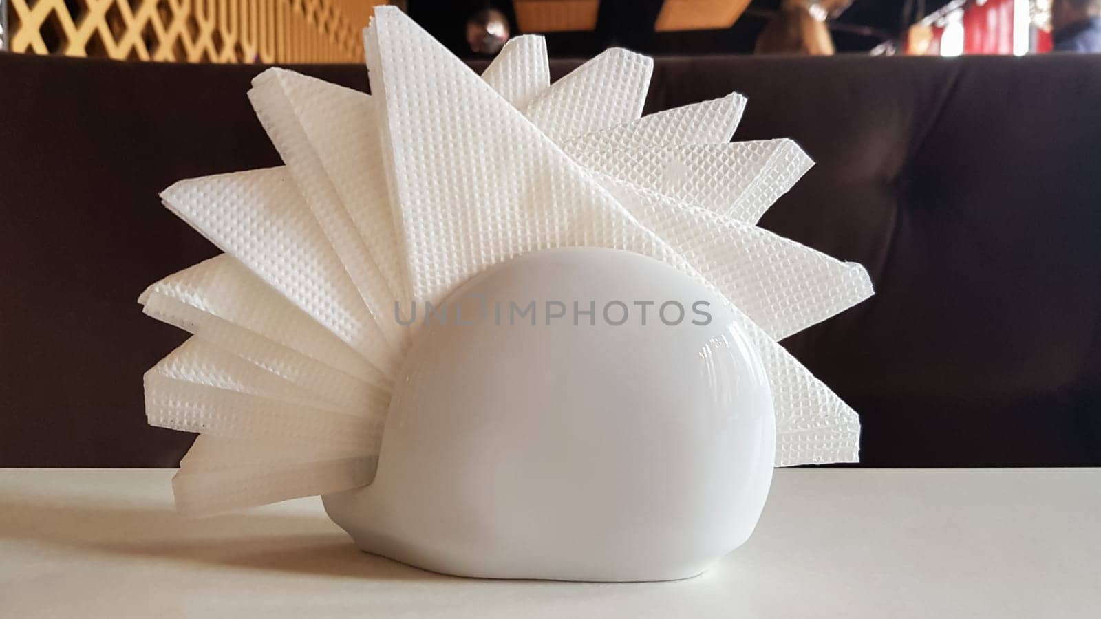 A table in a cafe and restaurant. White napkins in a ceramic napkin holder. Hotel dining table with napkins. A paper napkin is placed in a glass on a table in the banquet room