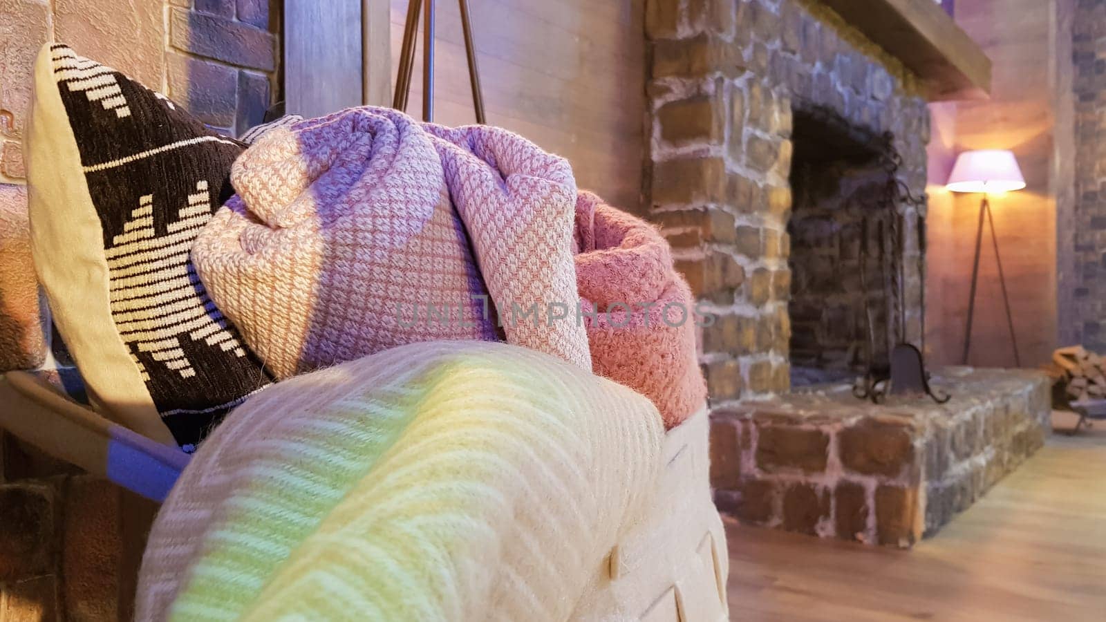 Knitted and warm blankets are folded and laid in a wicker basket near the fireplace. Cozy interior in the house. Details of a modern cozy interior.