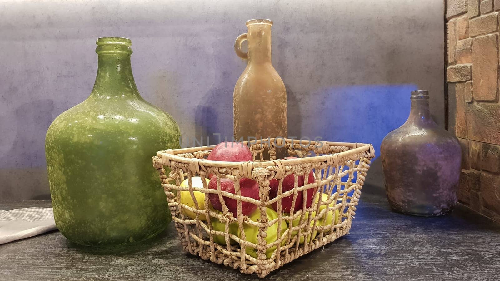 Large glass vases, a basket with apples and plates in the interior of a modern kitchen. The combination of wood and concrete in the design. Modern style dining kitchen.
