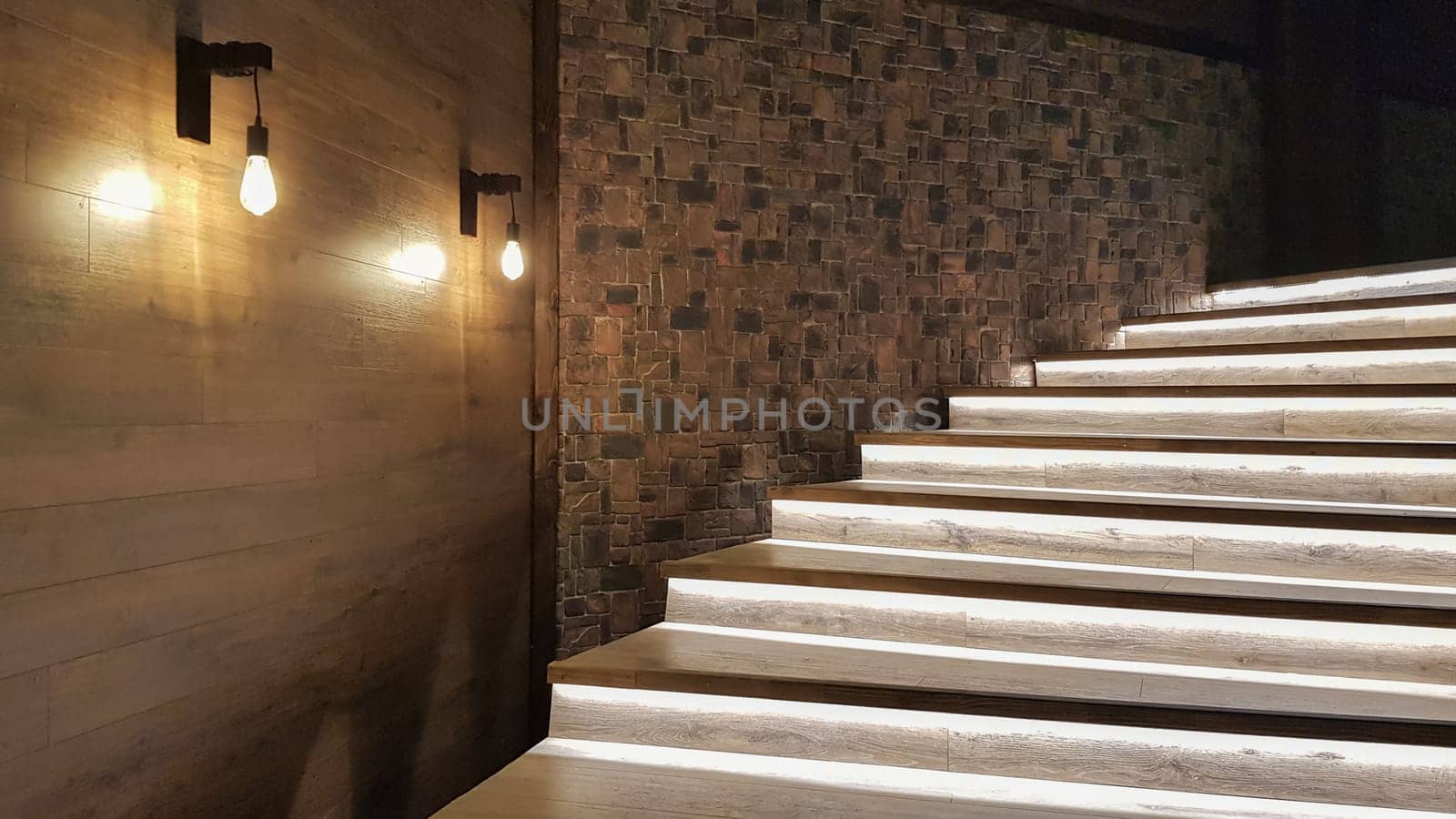 Illuminated staircase with wooden steps and illuminated at night in the interior of a large house.