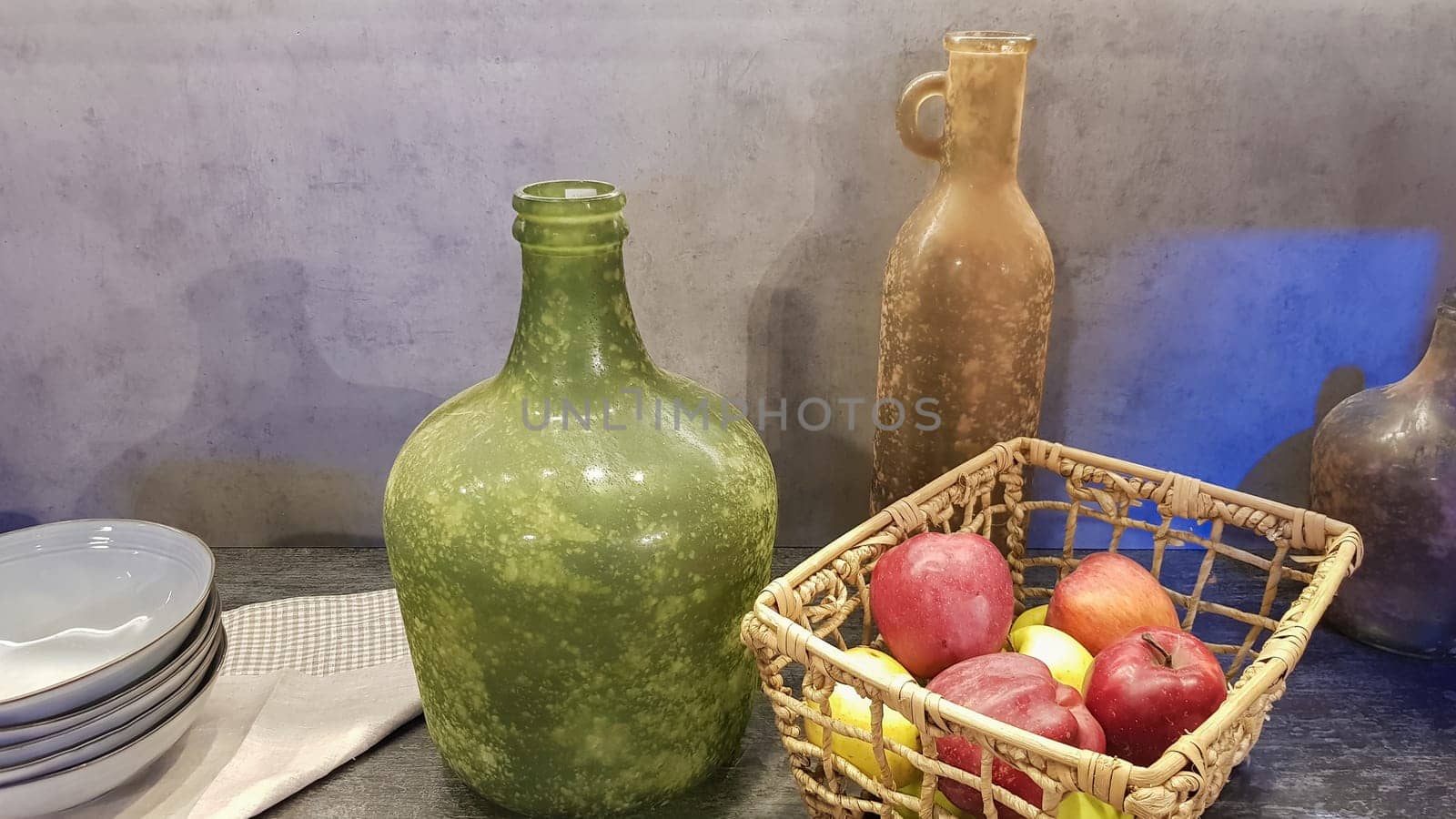 Large glass vases, a basket with apples and plates in the interior of a modern kitchen. The combination of wood and concrete in the design. Modern style dining kitchen.