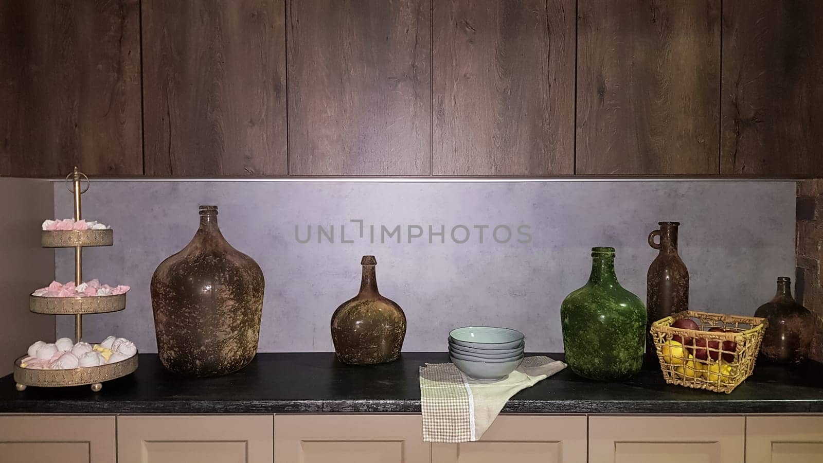 Large glass vases, a basket with apples and plates in the interior of a modern kitchen. The combination of wood and concrete in the design. Modern style dining kitchen.