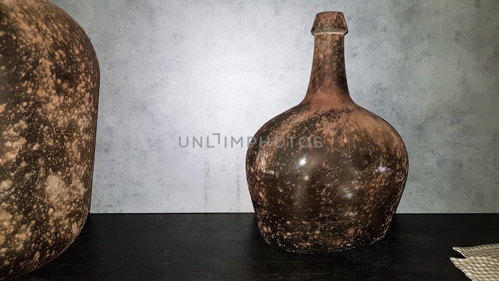 large vintage vases or jugs of colored glass as decoration elements in a modern interior near a gray concrete wall. Decoration of an apartment or house