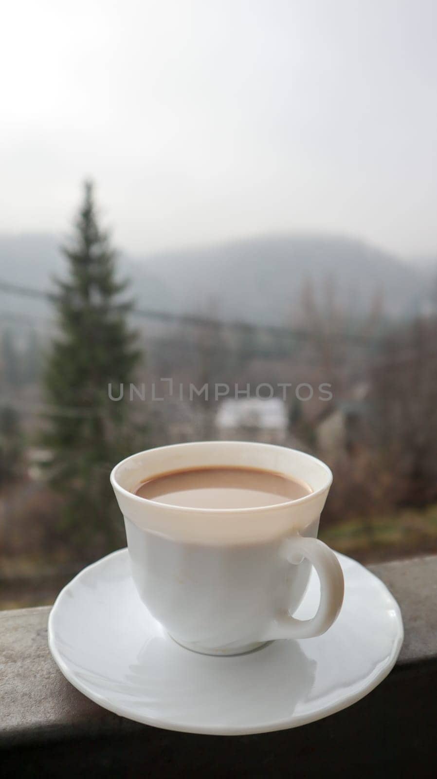 White cup of coffee on abstract nature background. One coffee mug on the balcony with a view of the nature behind. Ceramic cup with a drink on the hotel balcony.