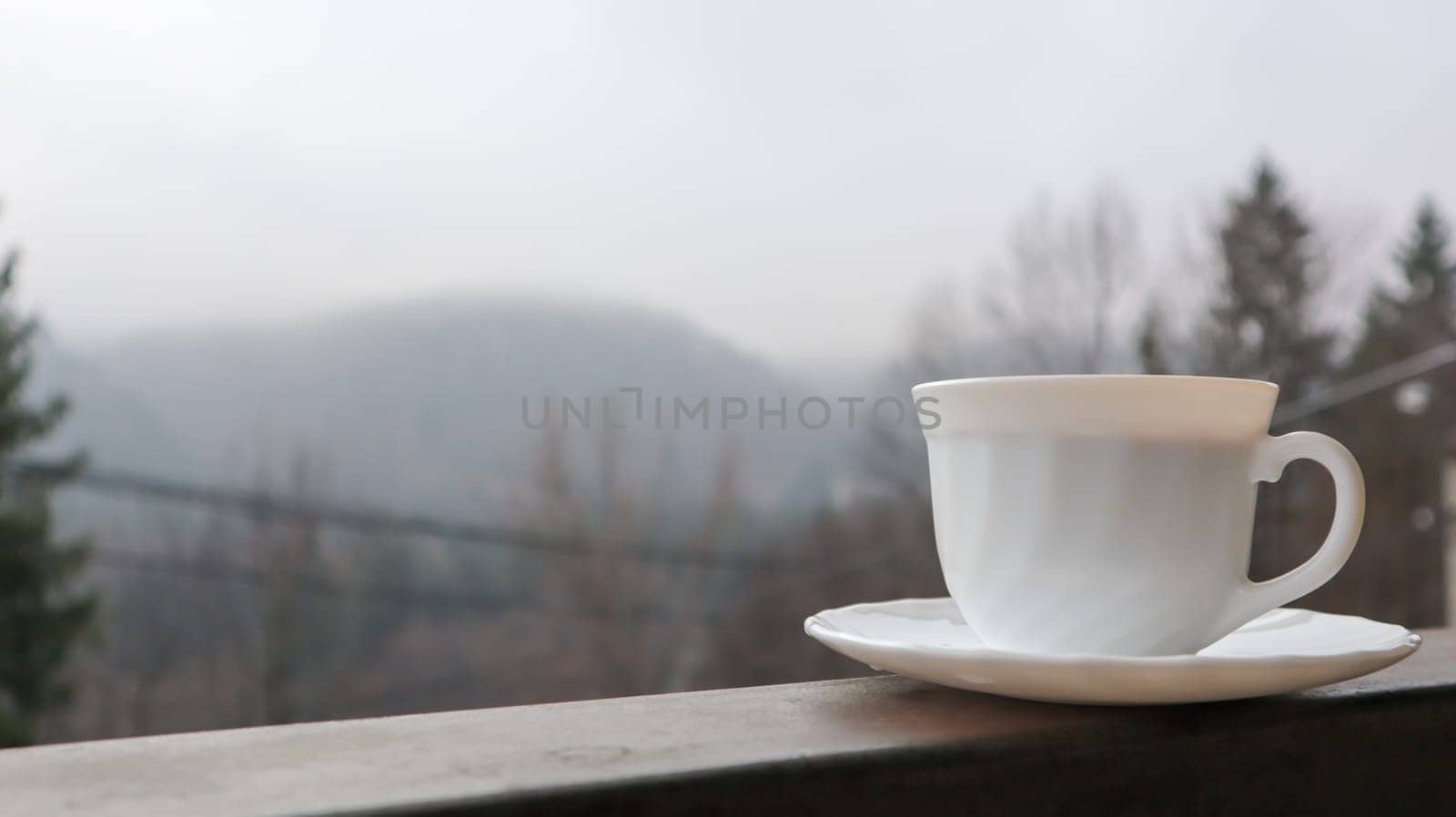 White cup of coffee on abstract nature background. One coffee mug on the balcony with a view of the nature behind. Ceramic cup with a drink on the hotel balcony.