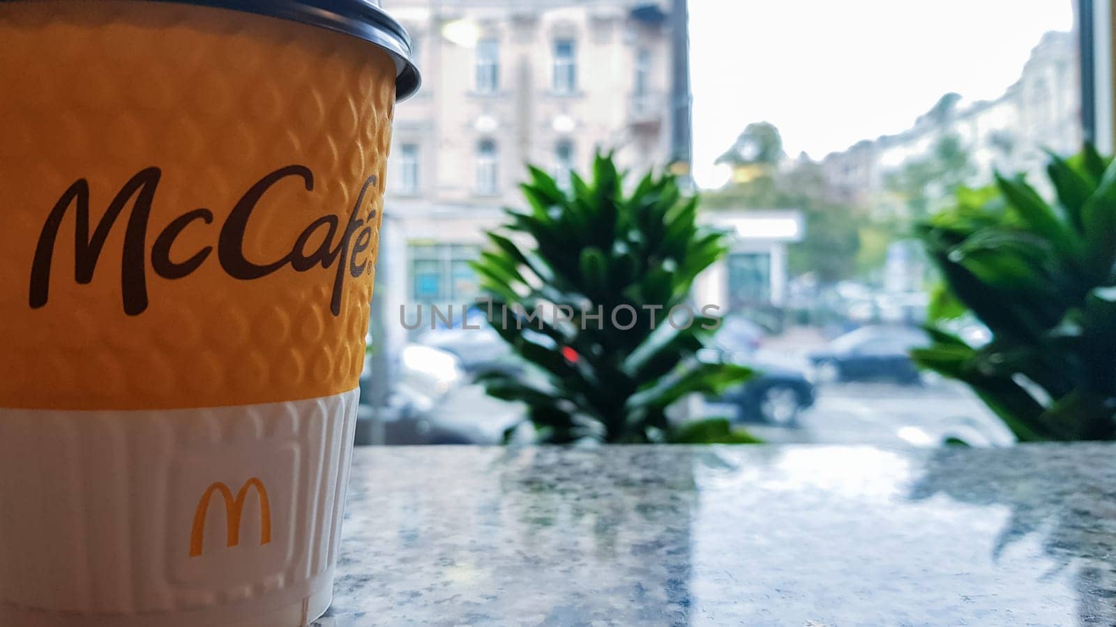 McDonald's logo on a yellow paper cup with hot McCafe coffee near the window. Fast food chain. Breakfast, coffee time. Ukraine, Kiev - September 30, 2020