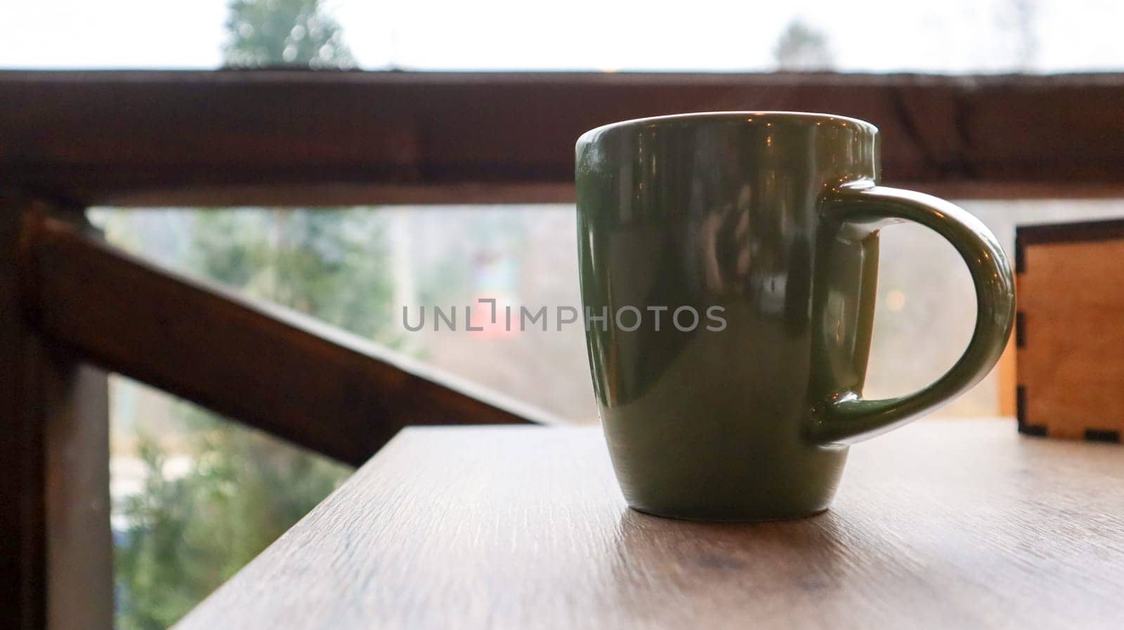 Green cup with tea or coffee on a wooden table on the balcony overlooking the street. Hot drink on the table on the veranda of the summer cafe. Soft focus