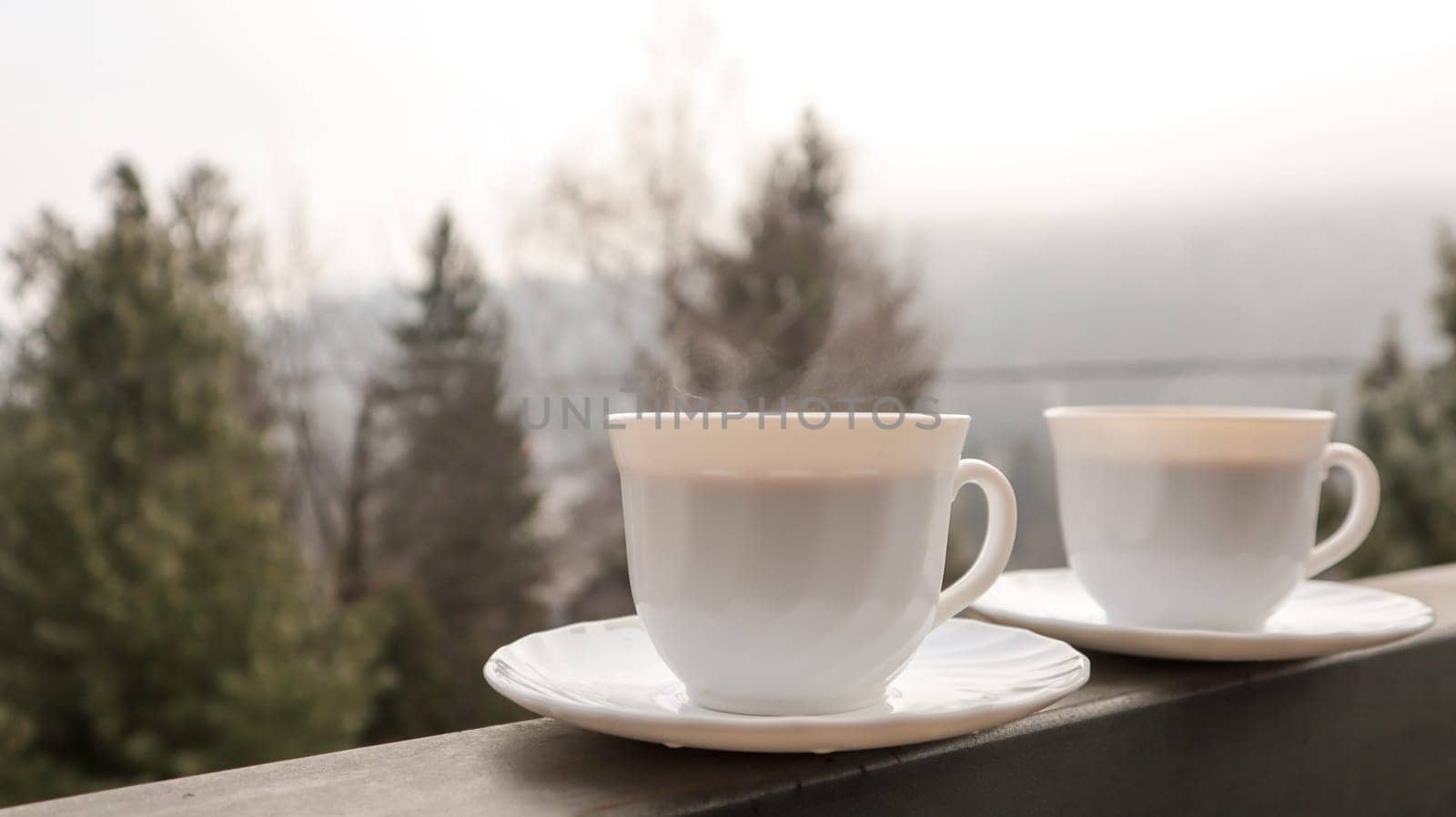 Two coffee cups on a balcony with mountain landscape in the morning. Two cups of morning coffee, standing on the side of the balcony, with a magical view of the autumn forests