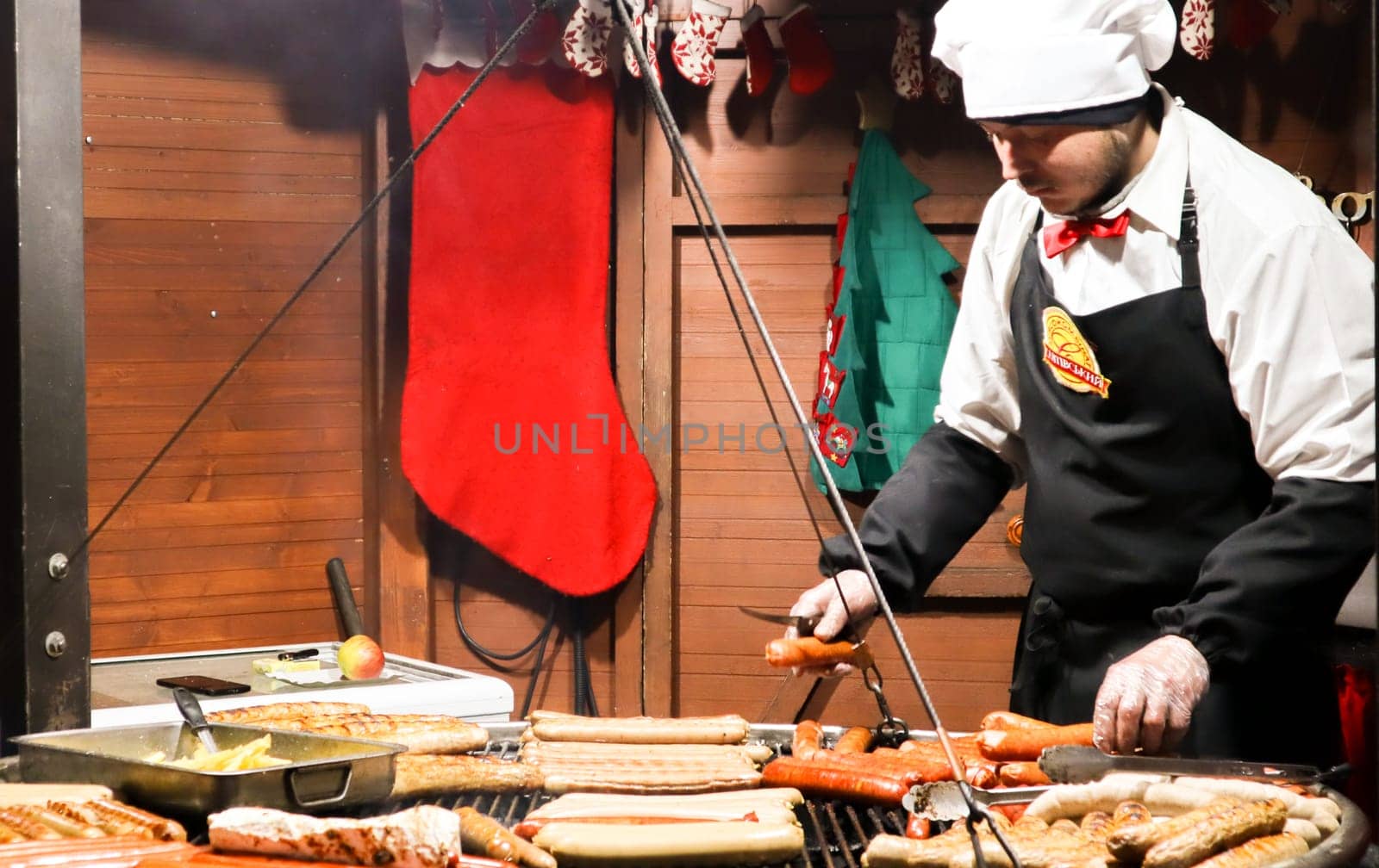 Ukraine, Kiev - January 3, 2019: a chef cooks a barbecue on the grill, street food, food festival. Fresh sausage and grilled hot dogs outdoors. A man is preparing street food of German cuisine.