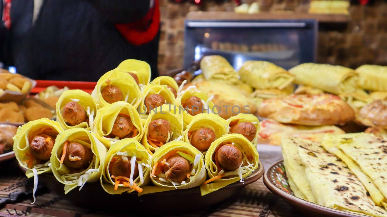 smoked sausage in pita bread on the window of a street fast food restaurant. Rack with trays with grilled sausages and hot dogs. Food at the street food festival. traditional food with sausages.