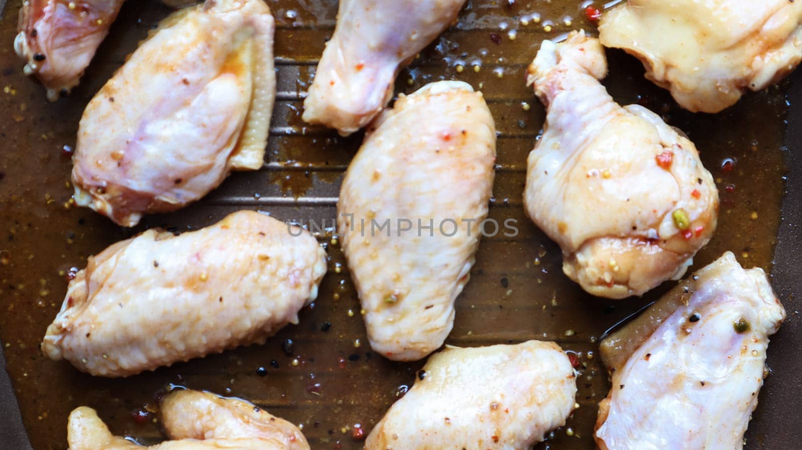 Raw pickled chicken teriyaki wings in a pan before frying. A few raw chicken wings on a baking sheet. Chicken meat in oil and in spices in a black pan, the cooking process