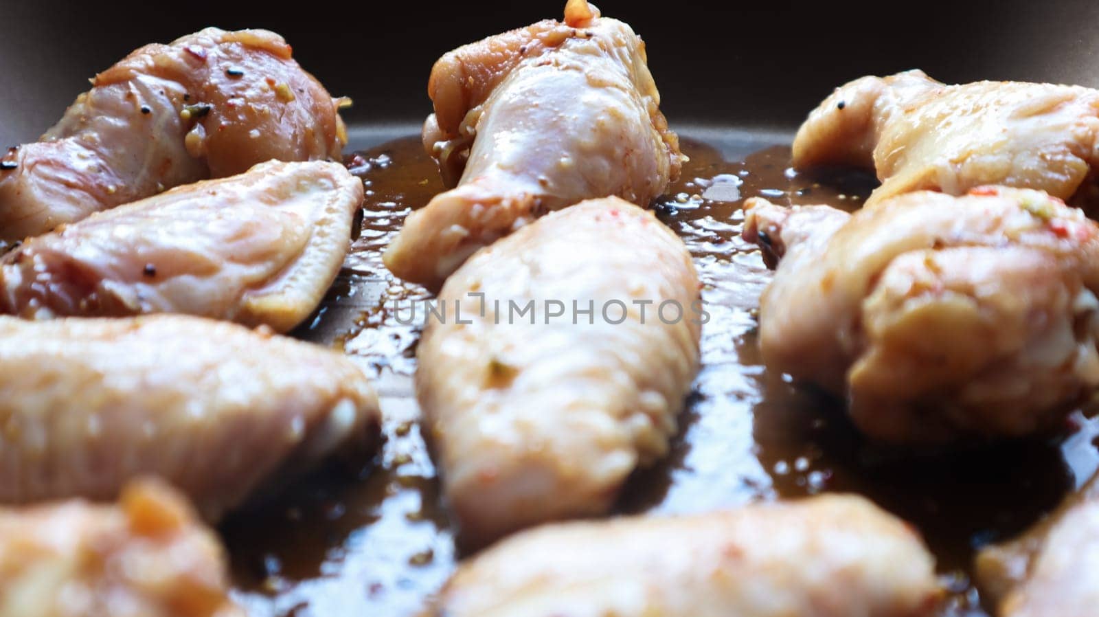 Raw pickled chicken teriyaki wings in a pan before frying. A few raw chicken wings on a baking sheet. Chicken meat in oil and in spices in a black pan, the cooking process