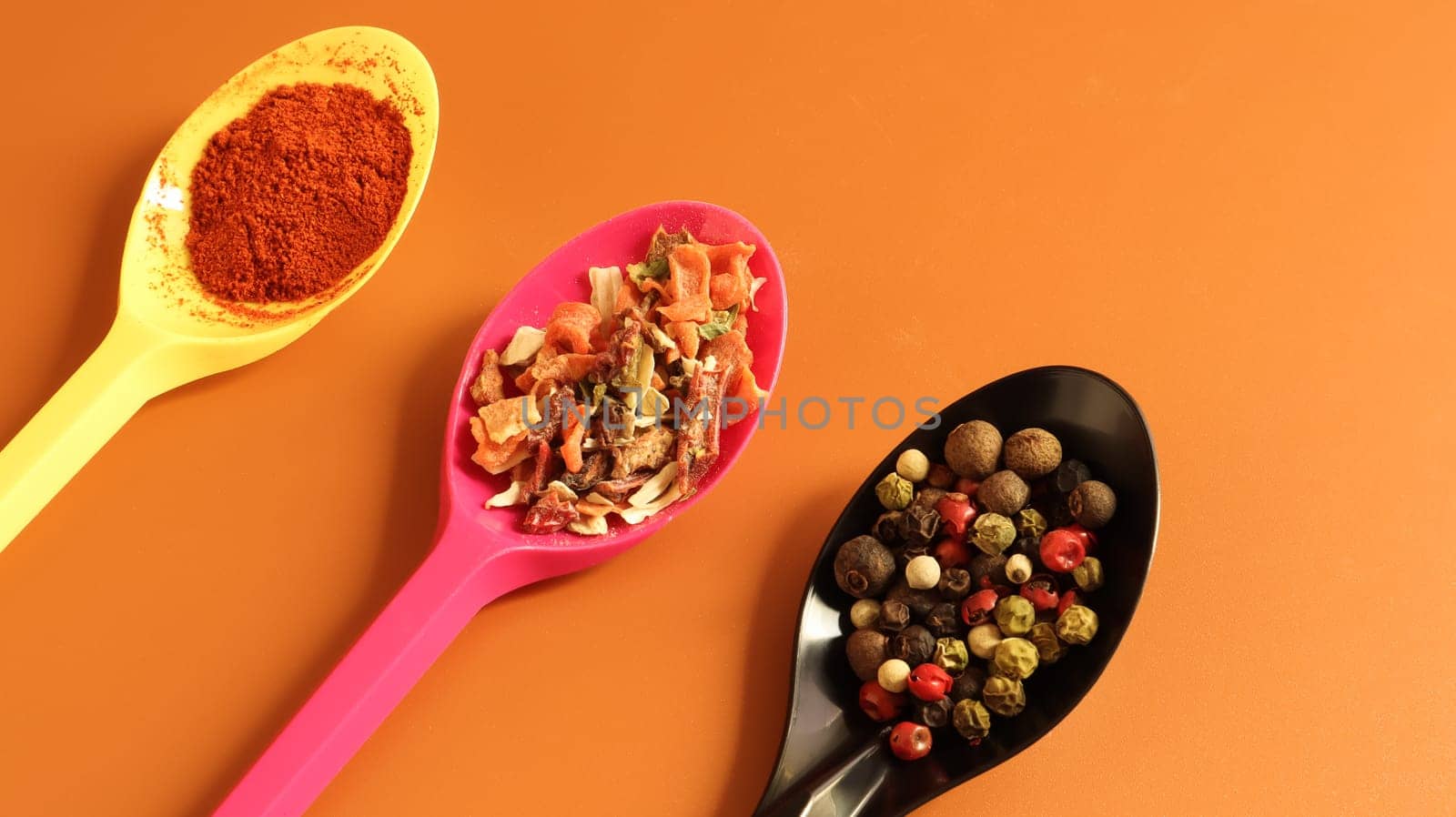 Various spices in plastic spoons on a brown background. Copy space. A mixture of peppers, red smoked paprika, seasoning twelve vegetables