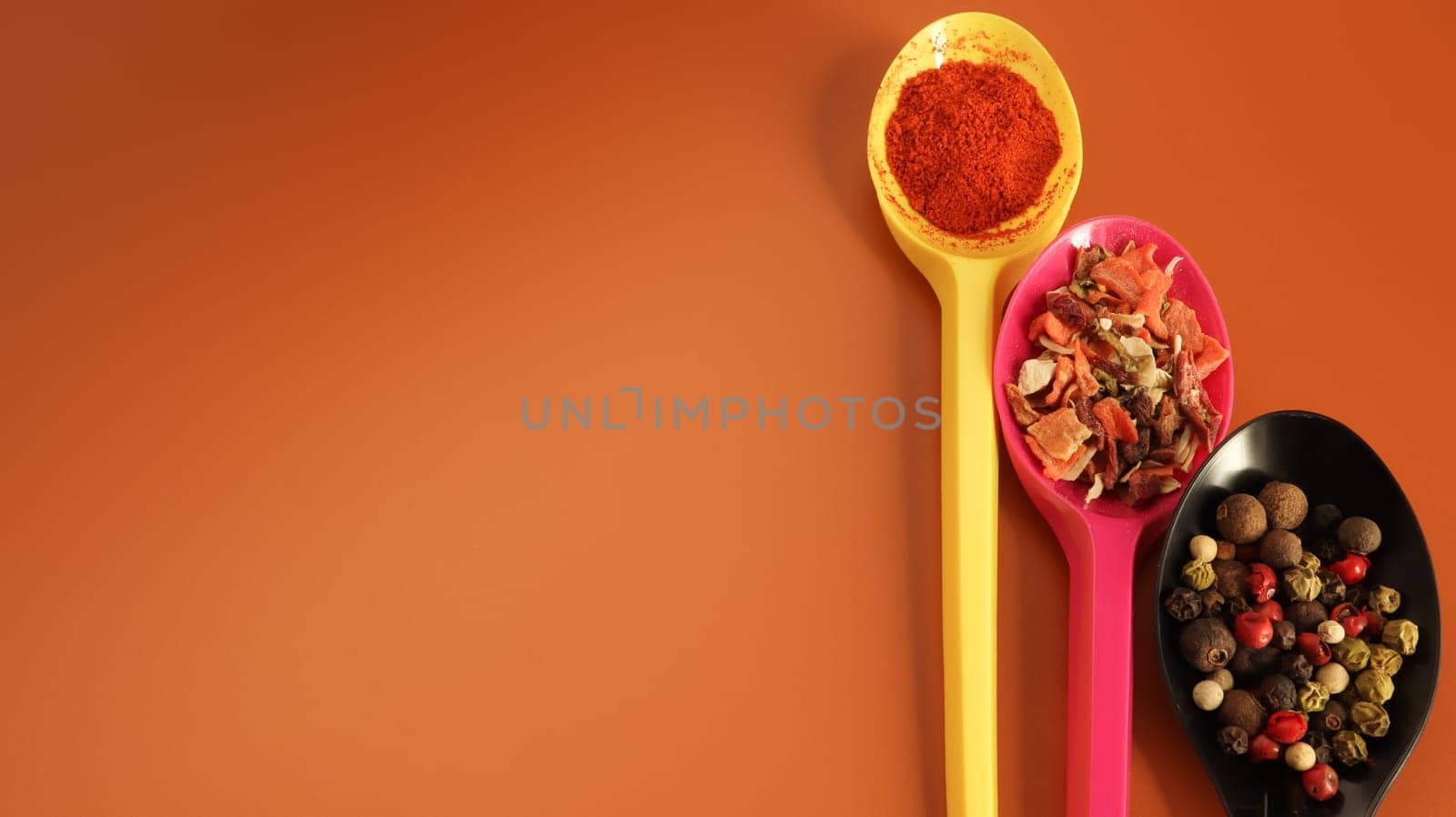 Various spices in plastic spoons on a brown background. Copy space. A mixture of peppers, red smoked paprika, seasoning twelve vegetables