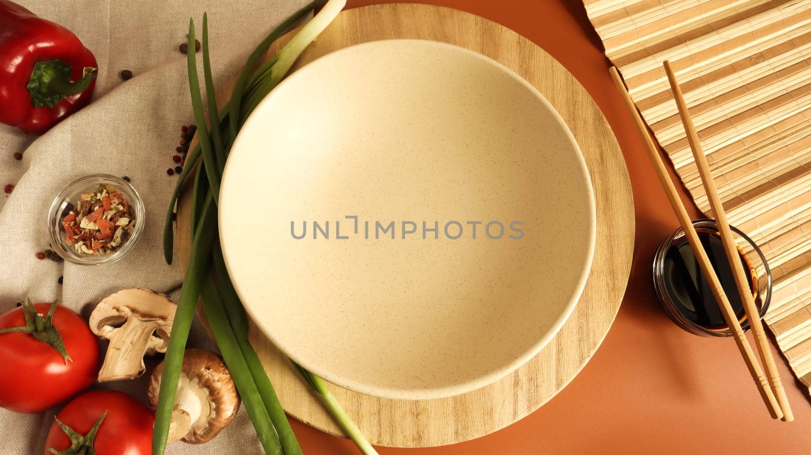 Round wooden board and plate, sauce and various vegetables on the table, wooden stick on a brown background. Flat lay. Copy space in the center of the frame for your text or logo. Recipe and Cooking.