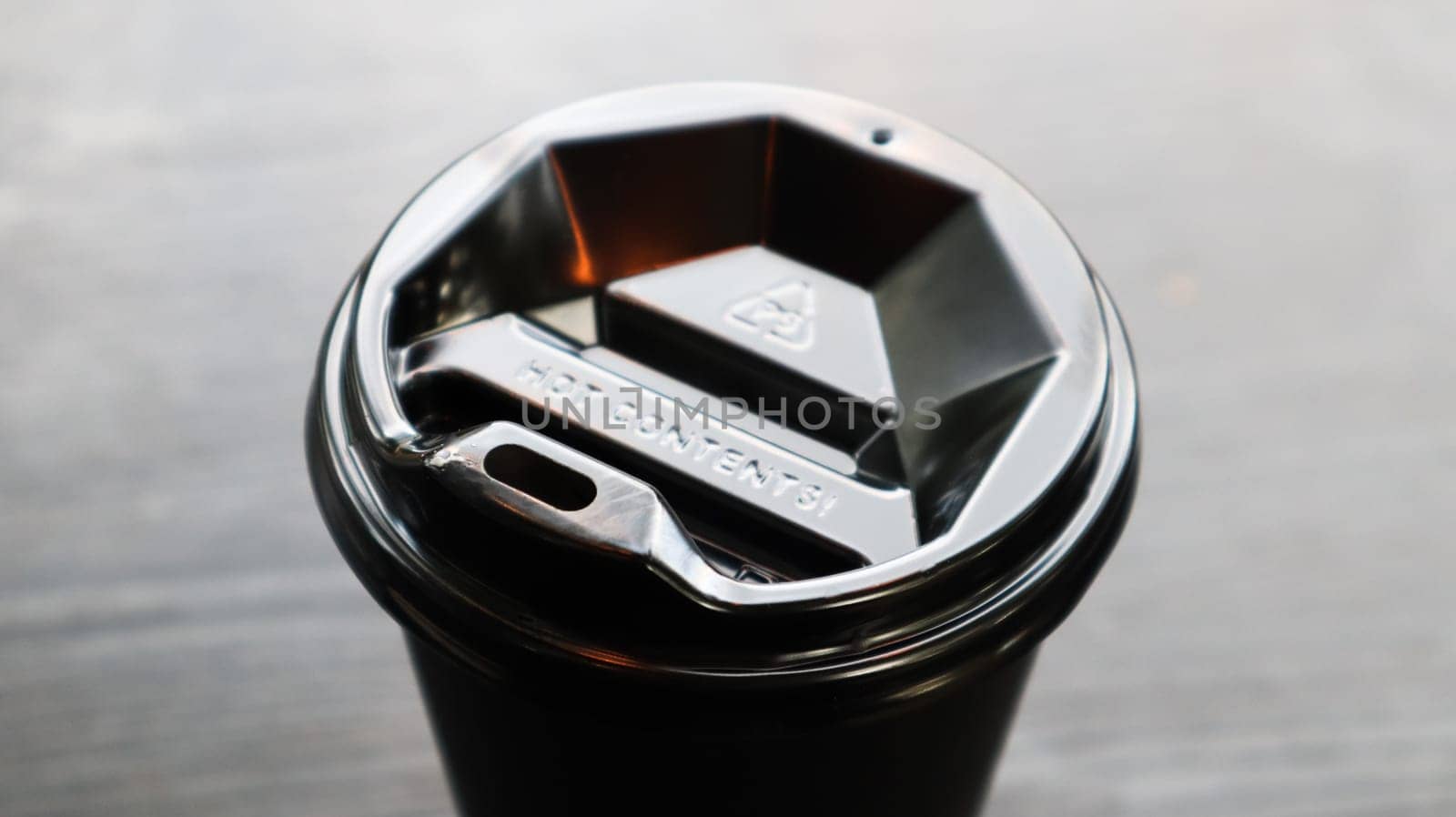 Black plastic coffee cup cover, top view. Takeaway coffee cup black background. Disposable cup close-up on a wooden table. Minimalist style.