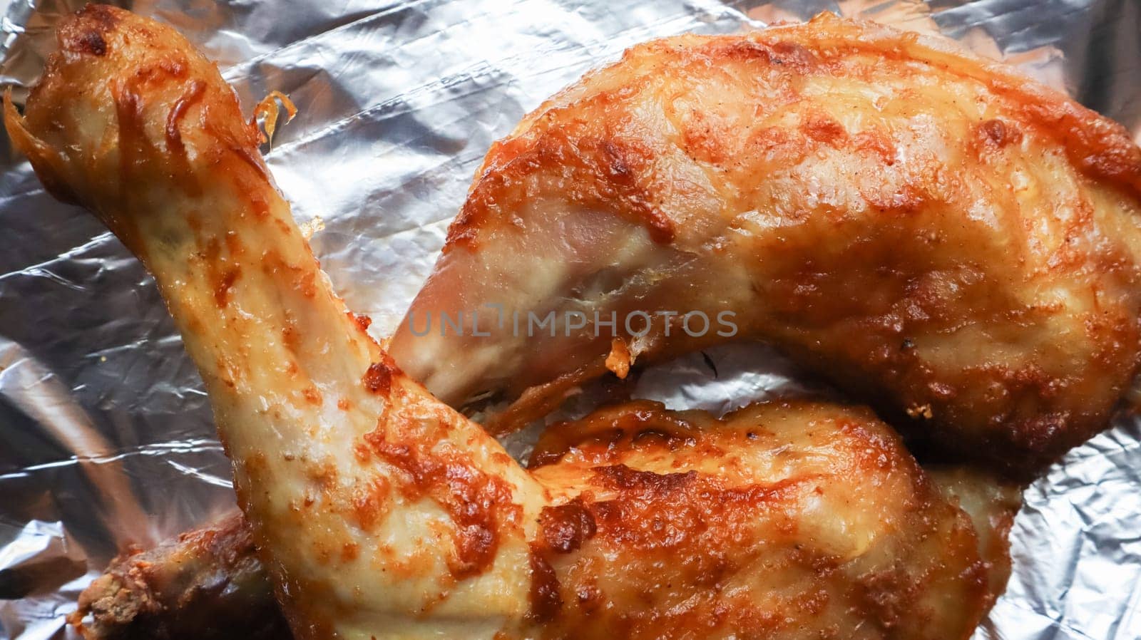 Two glazed chicken quarters, grilled legs on foil close-up. horizontal top view