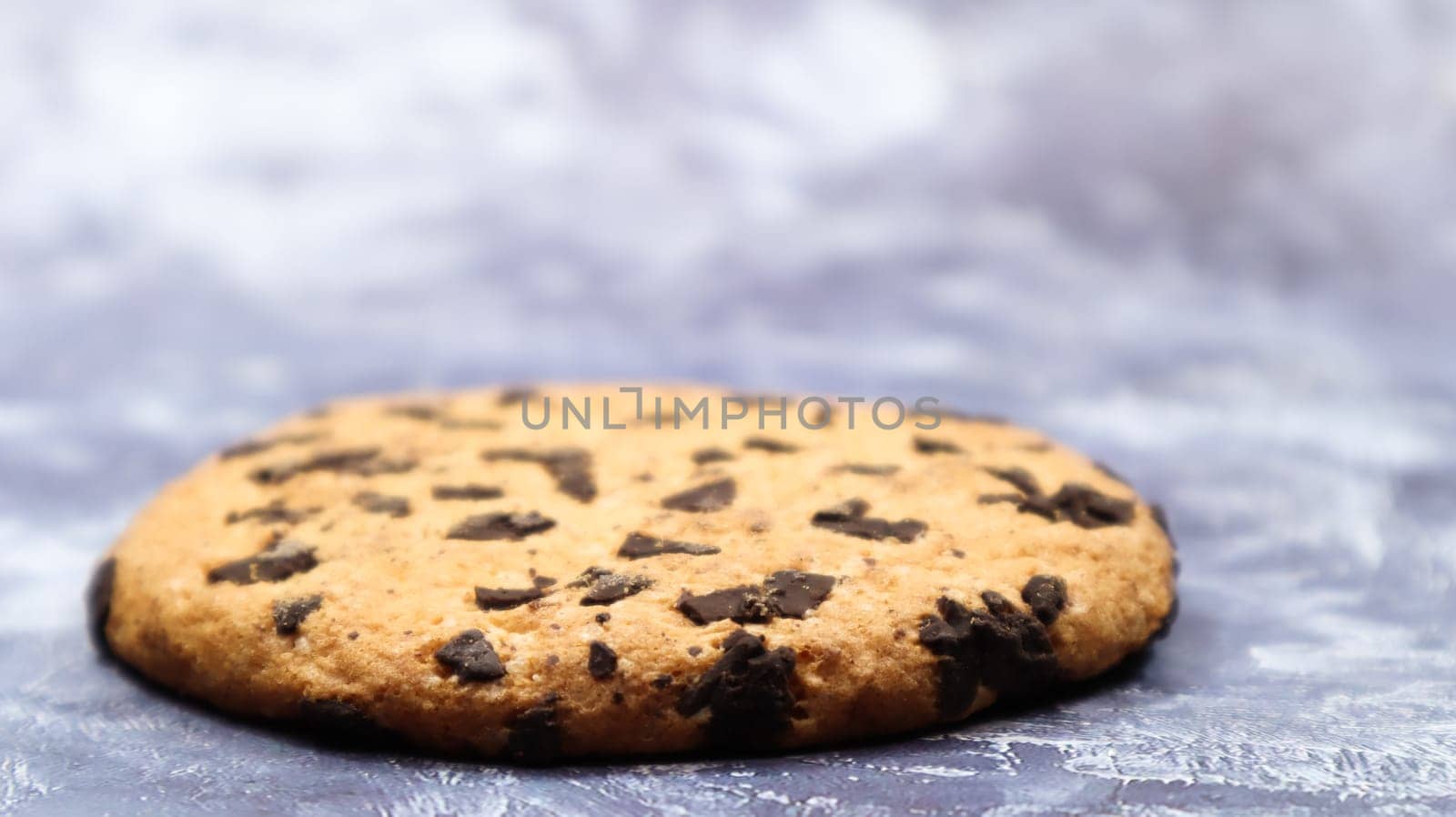 One soft, freshly baked chocolate chip cookie on a gray marble kitchen countertop. American traditional dessert. Delicious sweet food. Homemade baking concept for the holiday. Culinary background.