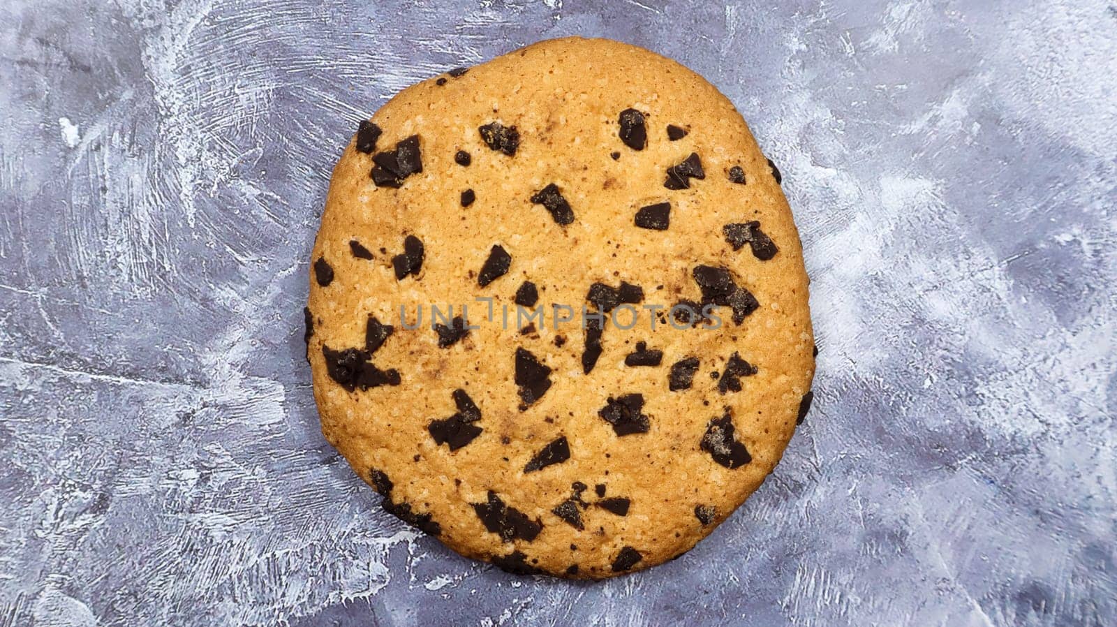 One soft, freshly baked chocolate chip cookie on a gray marble kitchen countertop. American traditional pastry, dessert. Delicious sweet food. Flat lay.