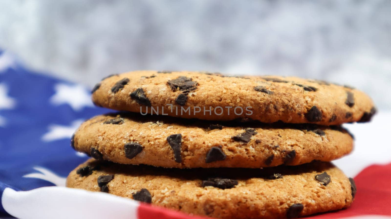 Patriotic cookies. Three rounded traditional chocolate chip cookies on the background of the flag of the United States of America. Delicious sweet pastries, dessert. America's favorite treat