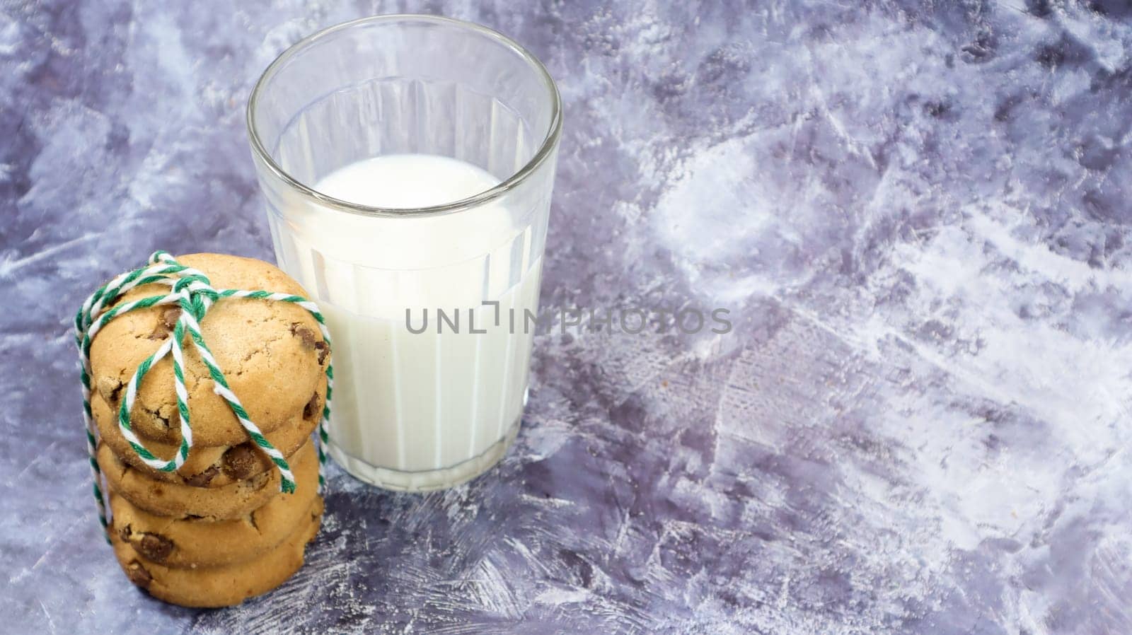 American chocolate chip cookies stacked on top of each other with milk in a glass on a gray background. Traditional rounded crunchy dough with chocolate chips. Bakery. Delicious dessert, pastries