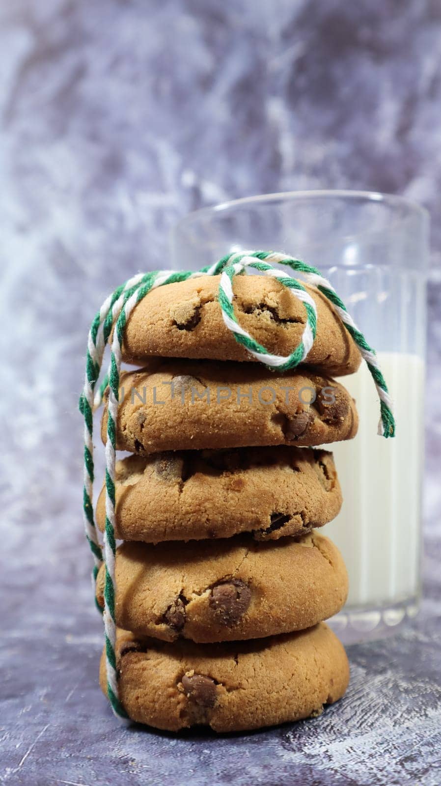 American chocolate chip cookies stacked on top of each other with milk in a glass on a gray background. Traditional rounded crunchy dough with chocolate chips. Bakery. Delicious dessert, pastries